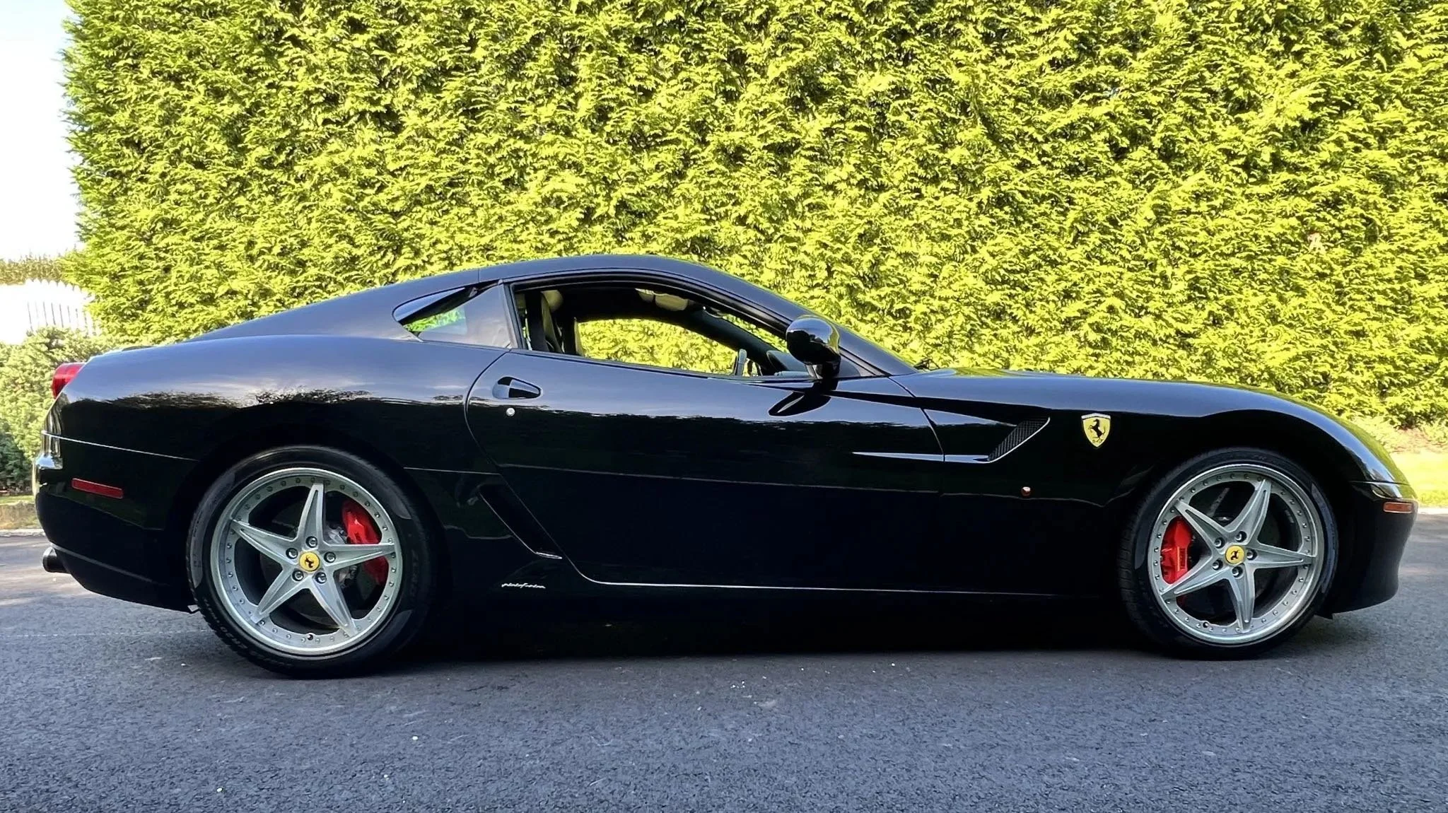 A black Ferrari sports car parked on the side of a road with green bushes in the background.