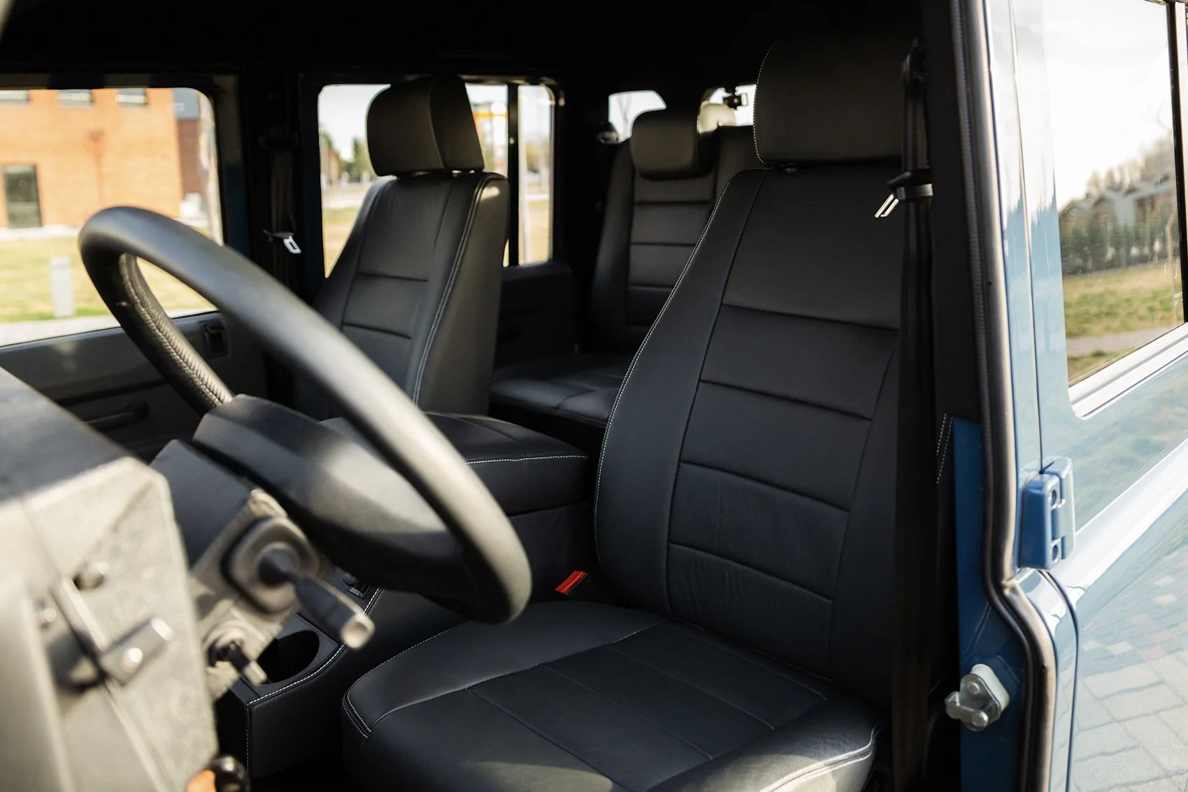 Interior of a vehicle with black seats, including two front seats and a back bench seat, visible through an open door.