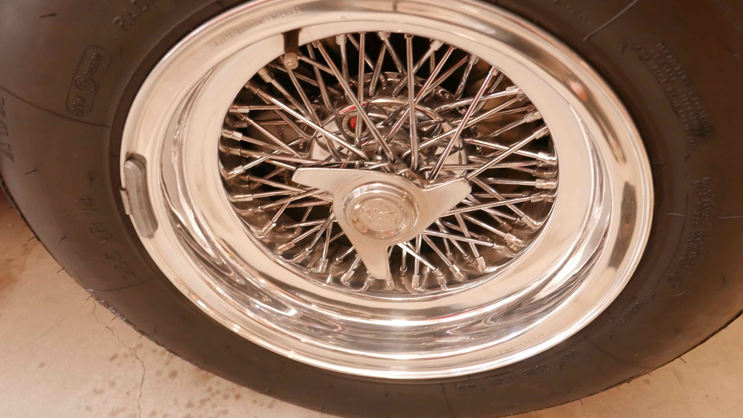 Close-up of a vintage wire-spoked car wheel with a chrome rim and black tire.
