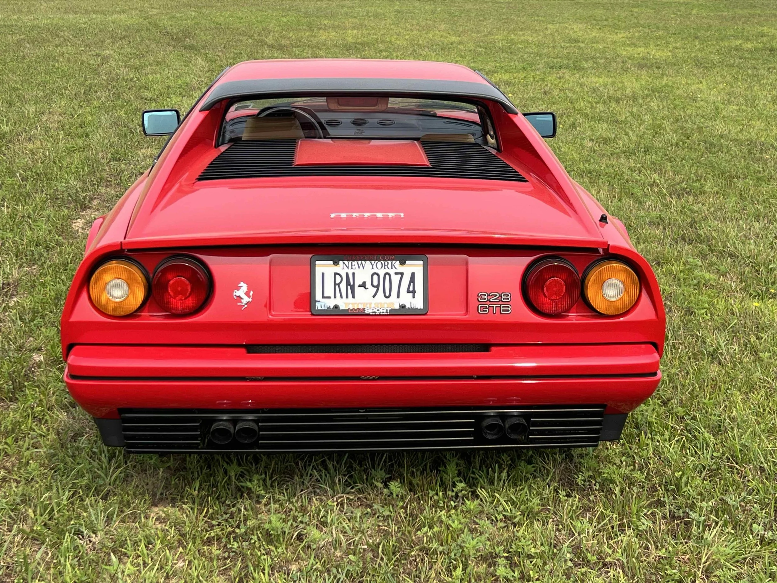 Red Ferrari 328 GTB parked on a grassy field, shown from the rear.