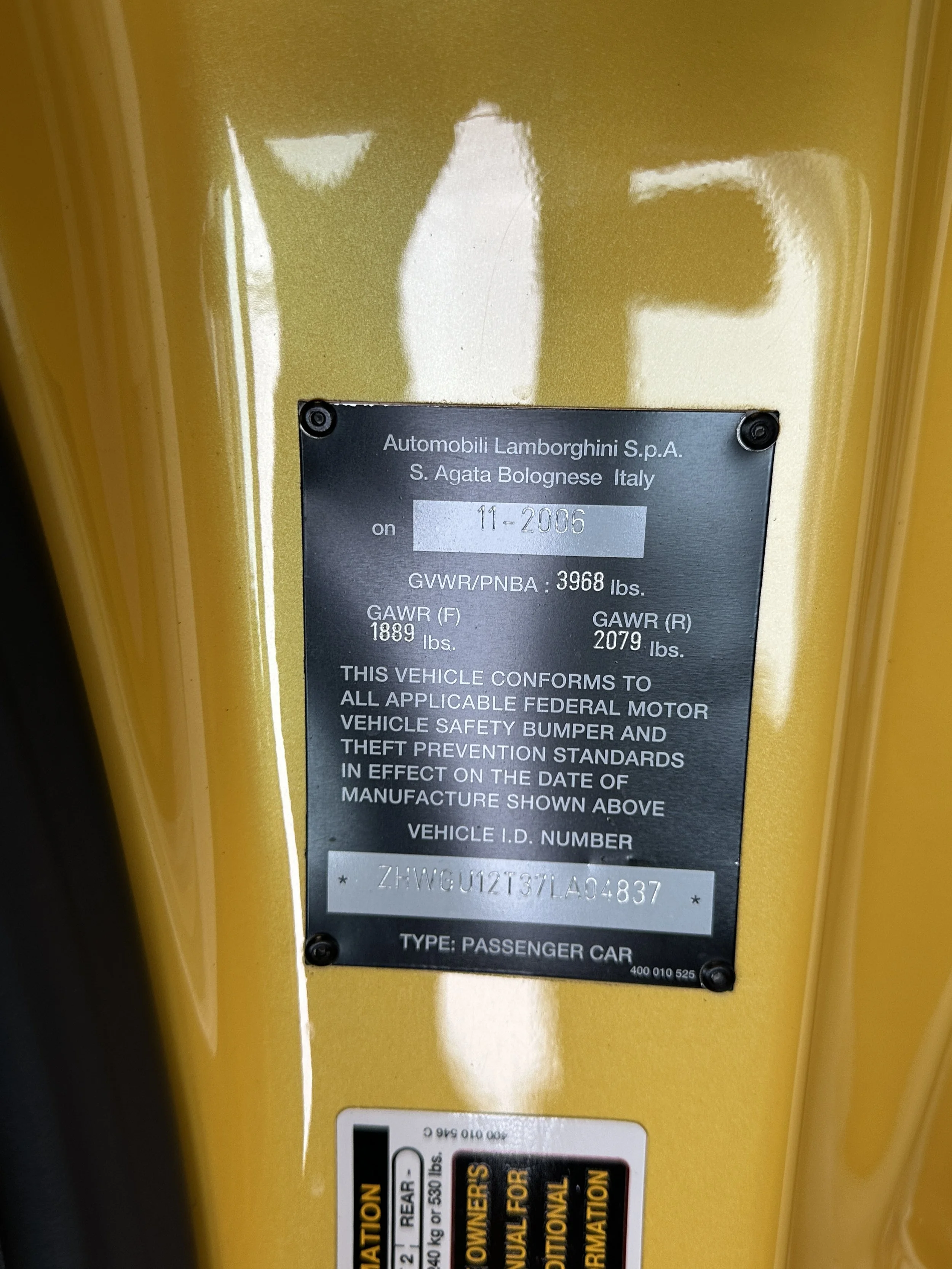 Close-up of a vehicle identification plate on a yellow Lamborghini, showing manufacture date November 2006, with vehicle specifications and identification number.