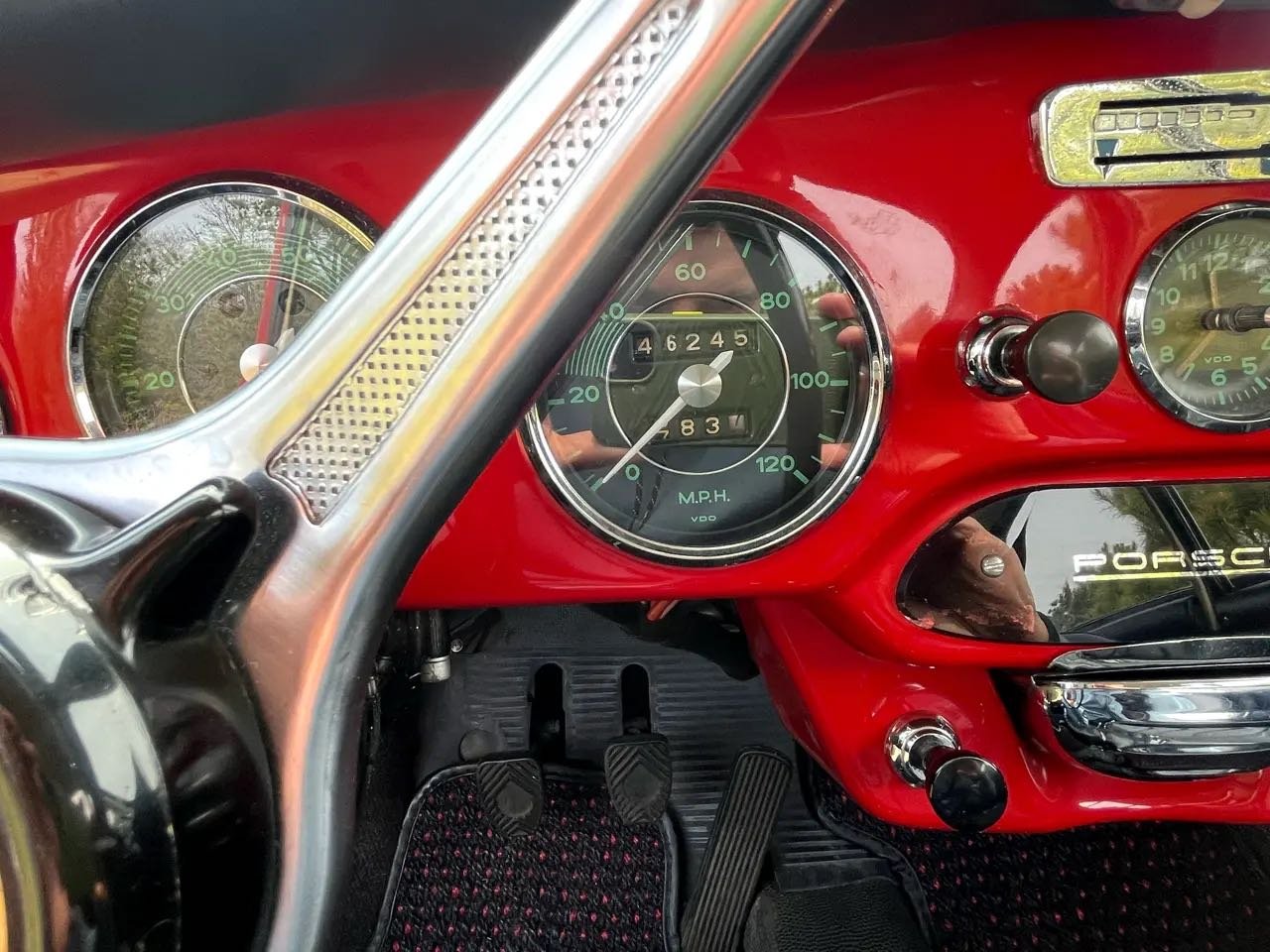 The dashboard of a classic red Porsche car showing the speedometer, odometer, and other gauges. The speedometer reads 0 miles per hour.