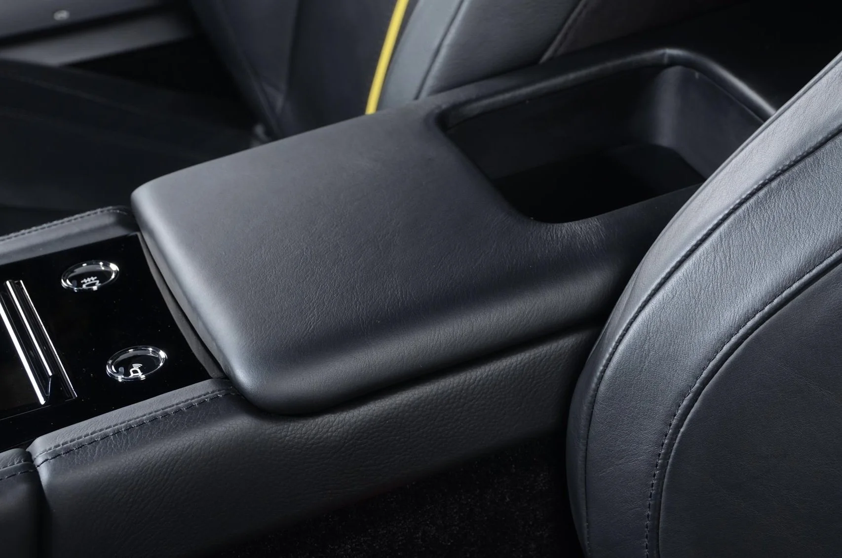 Close-up of a car's center console with a padded black cover and two control buttons, surrounded by black leather interior.