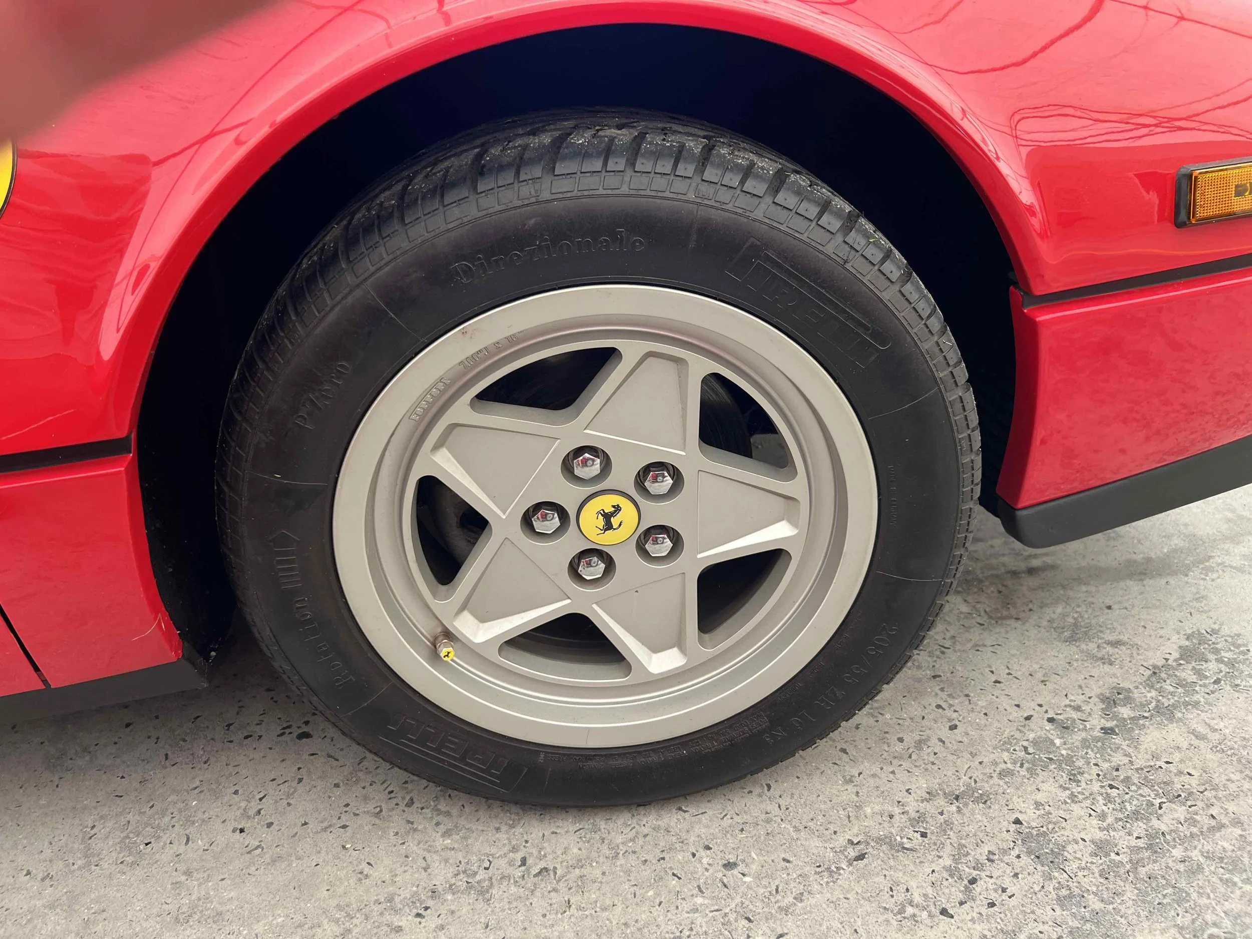 Close-up of a red sports car wheel with a silver five-spoke Rim featuring a yellow Ferrari emblem at the center, mounted on a black Pirelli tire.