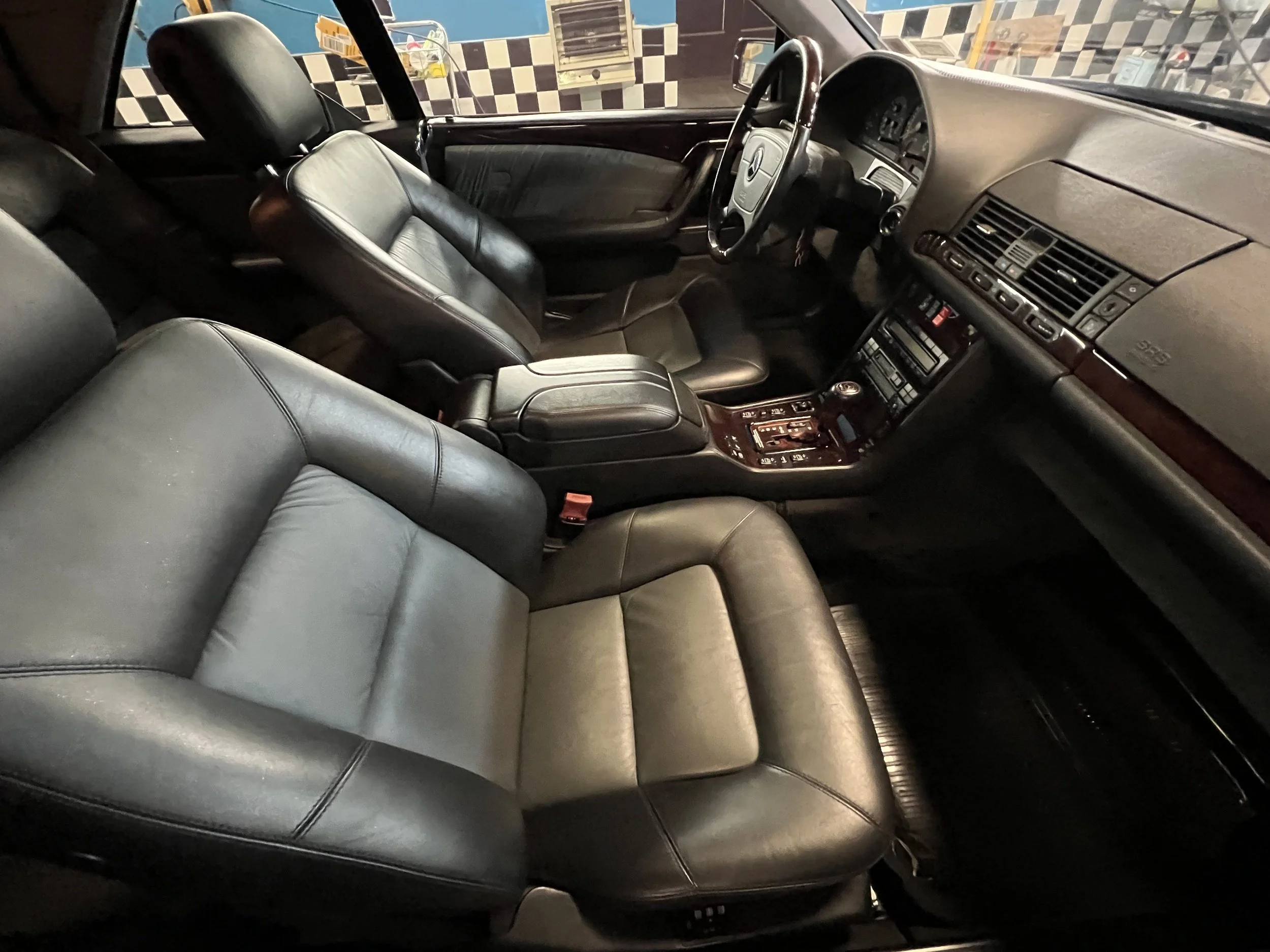 Interior of a classic luxury car with black leather seats, dashboard, and center console, viewed from the passenger side.
