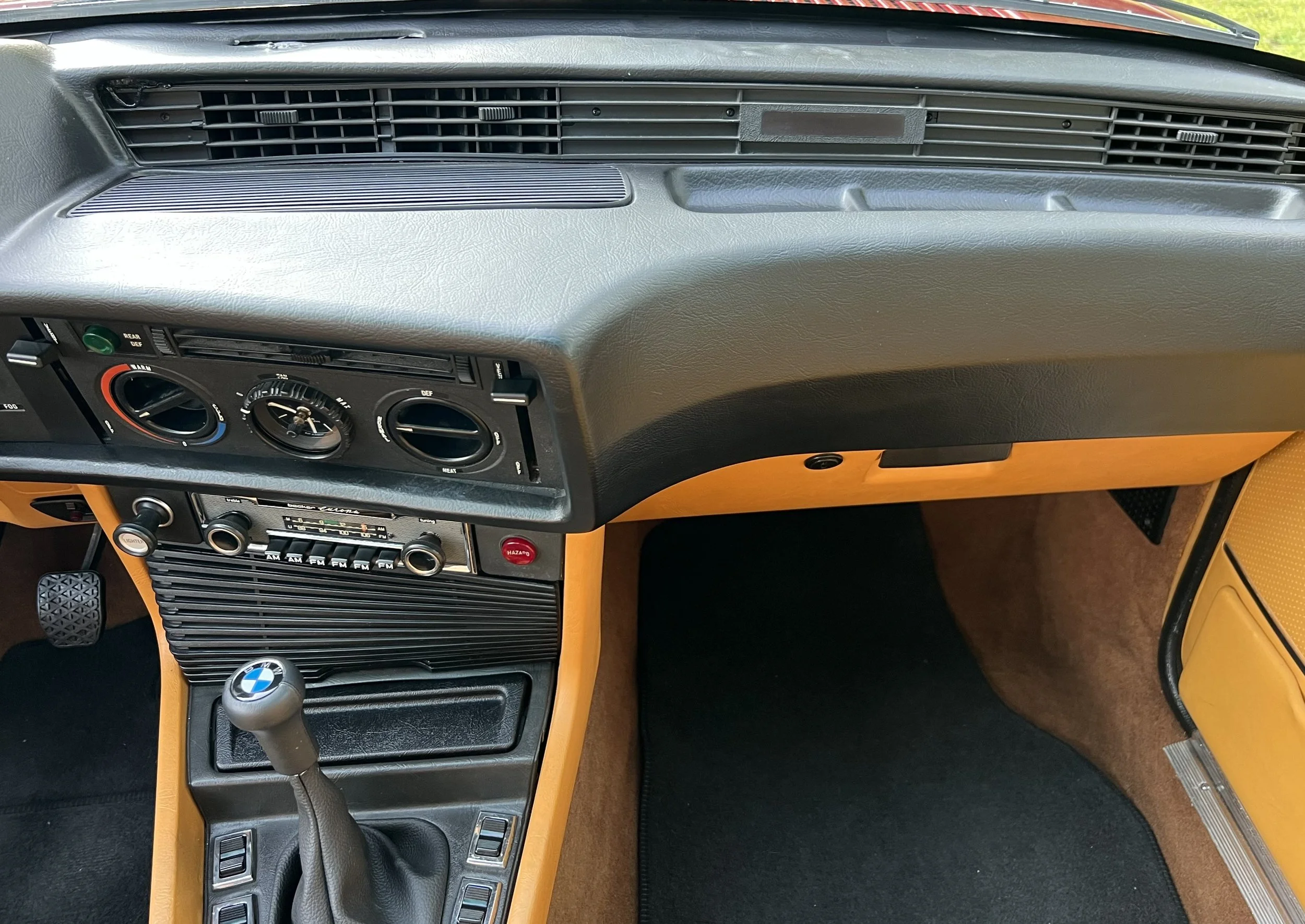 Interior of a vintage BMW BMW 630 csi car, showing the dashboard with air vents, climate controls, radio, and gear shift with BMW logo, yellow trim around the center console, and black floor mats.