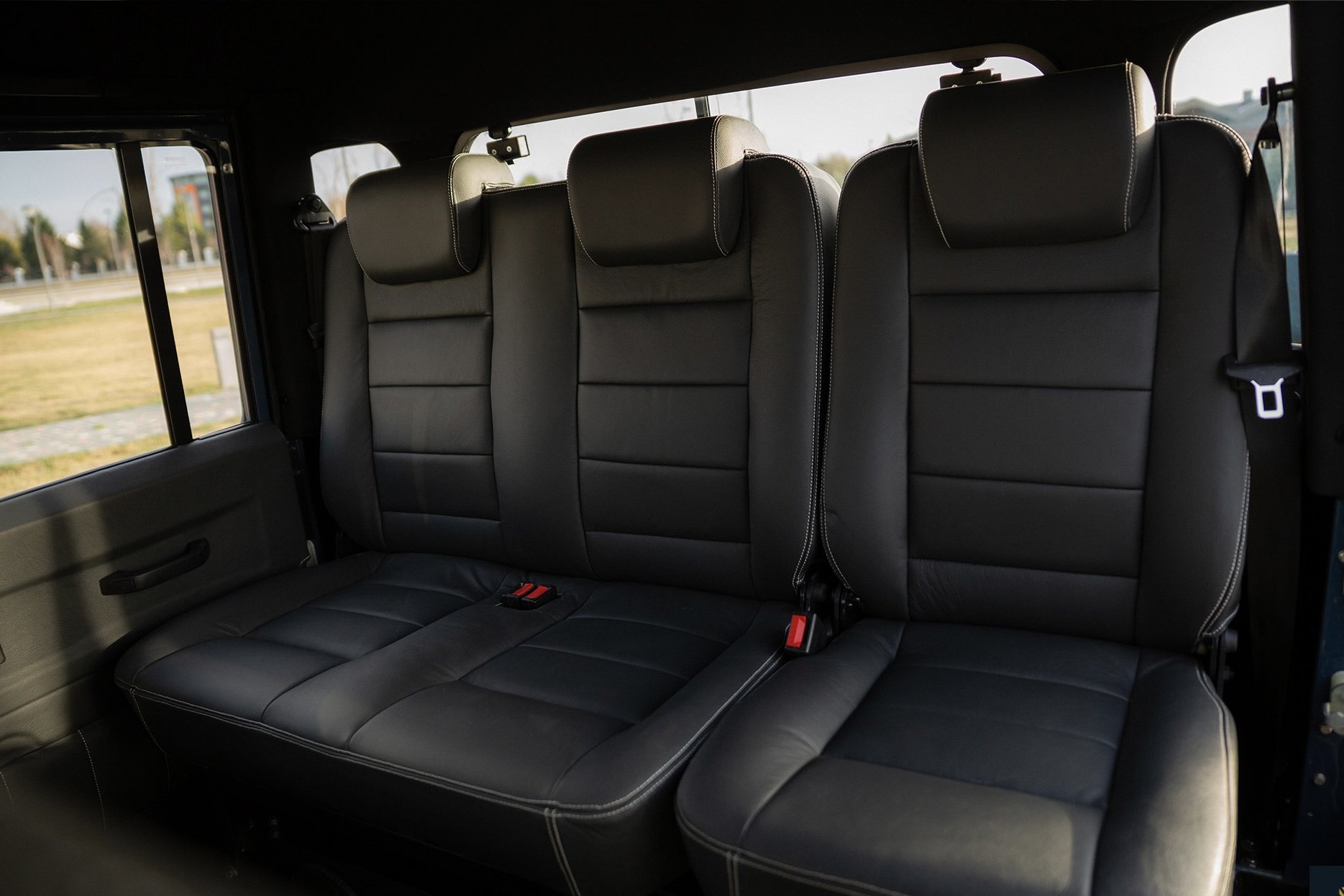 Interior of a vehicle showing three black leather seats with headrests and seat belts