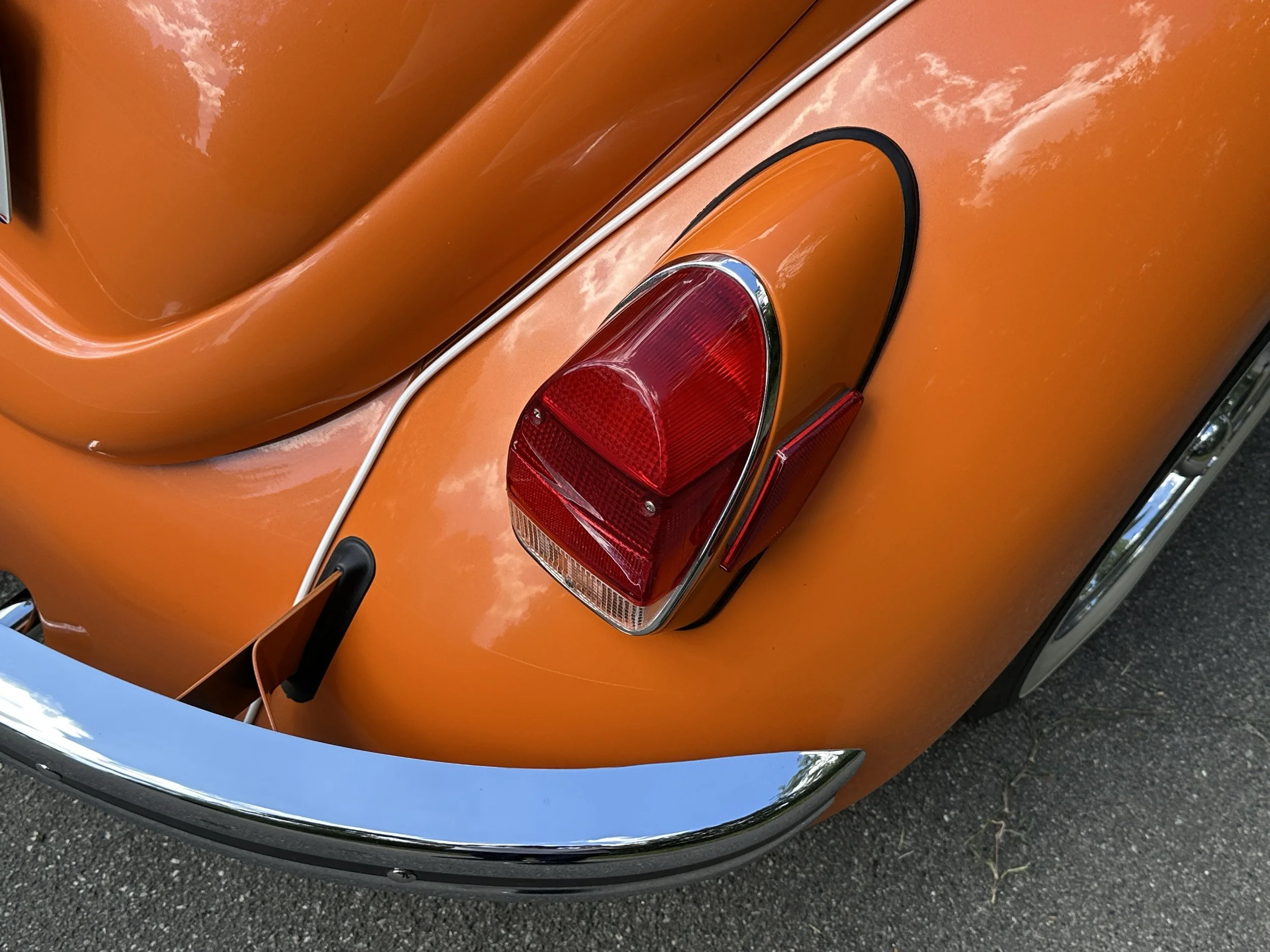 Close-up of the rear end of an orange classic car, showing a red tail light and chrome bumper.