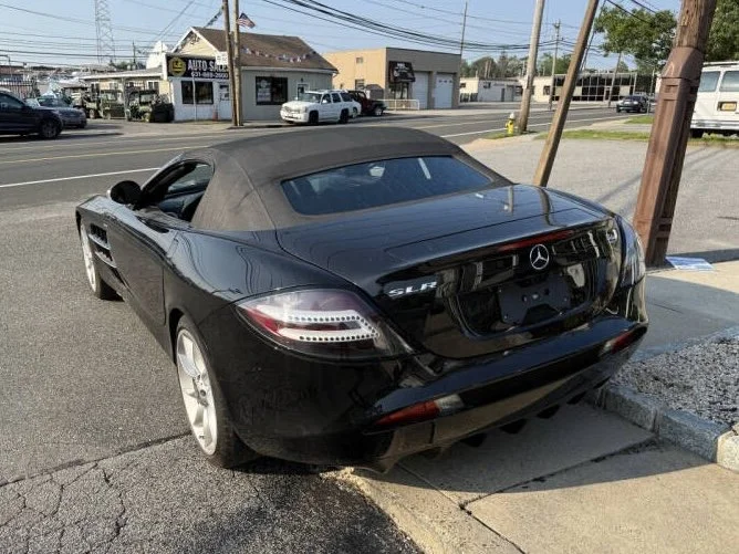 Black Mercedes-Benz SLK convertible parked on the side of the road near a leaning utility pole.