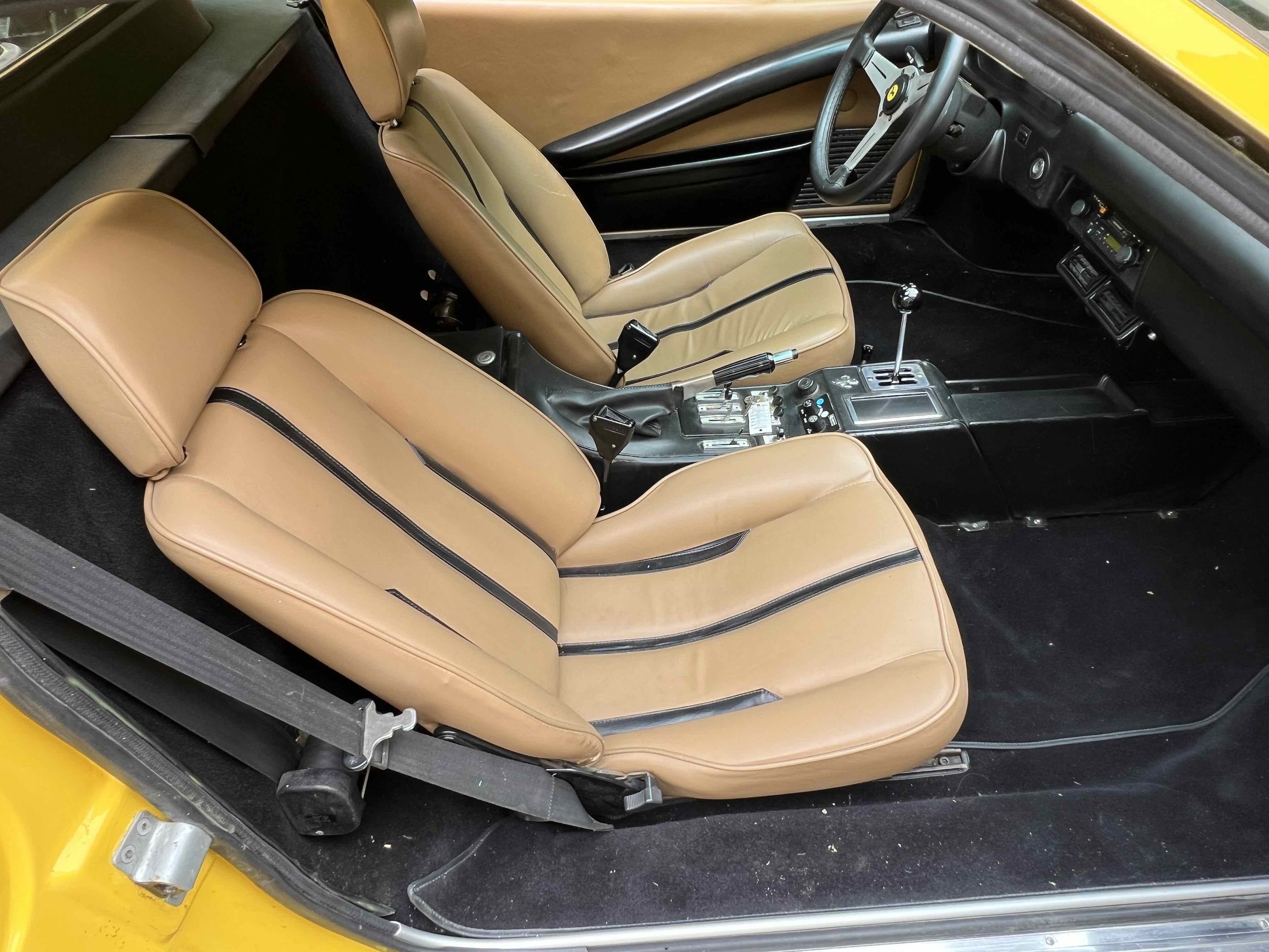 Interior of a vintage sports car with tan leather bucket seats, black center console, manual gear shifter, and a black dashboard with steering wheel.