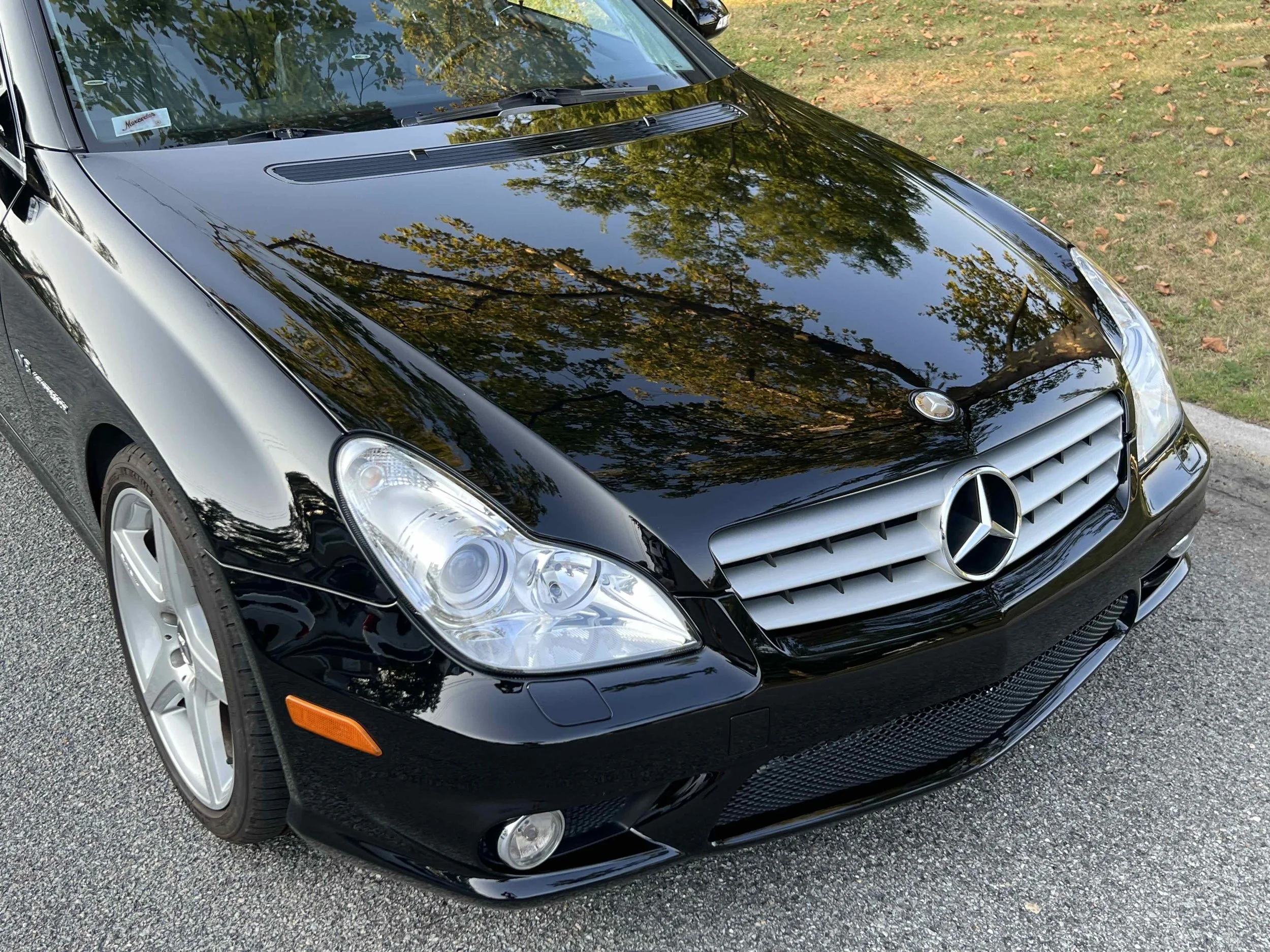 Black Mercedes-Benz car parked on street with tree reflections on the hood