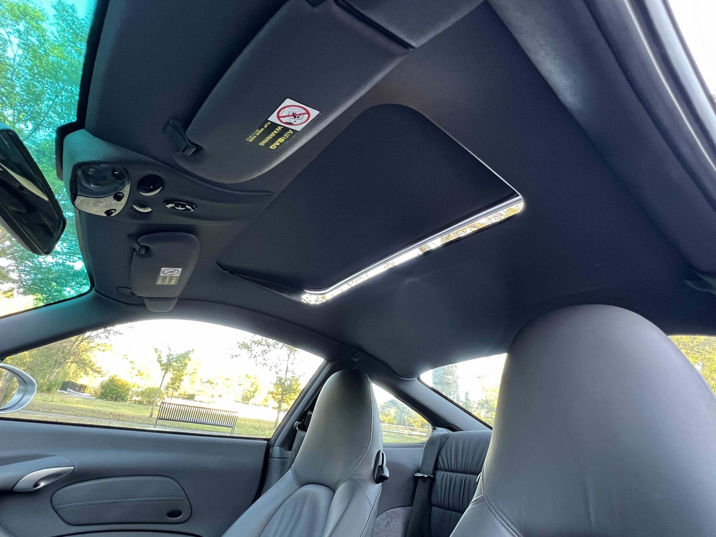 Interior of a vehicle showing the front and back seats, sunroof, and part of the dashboard, with trees and a park visible through the windows.