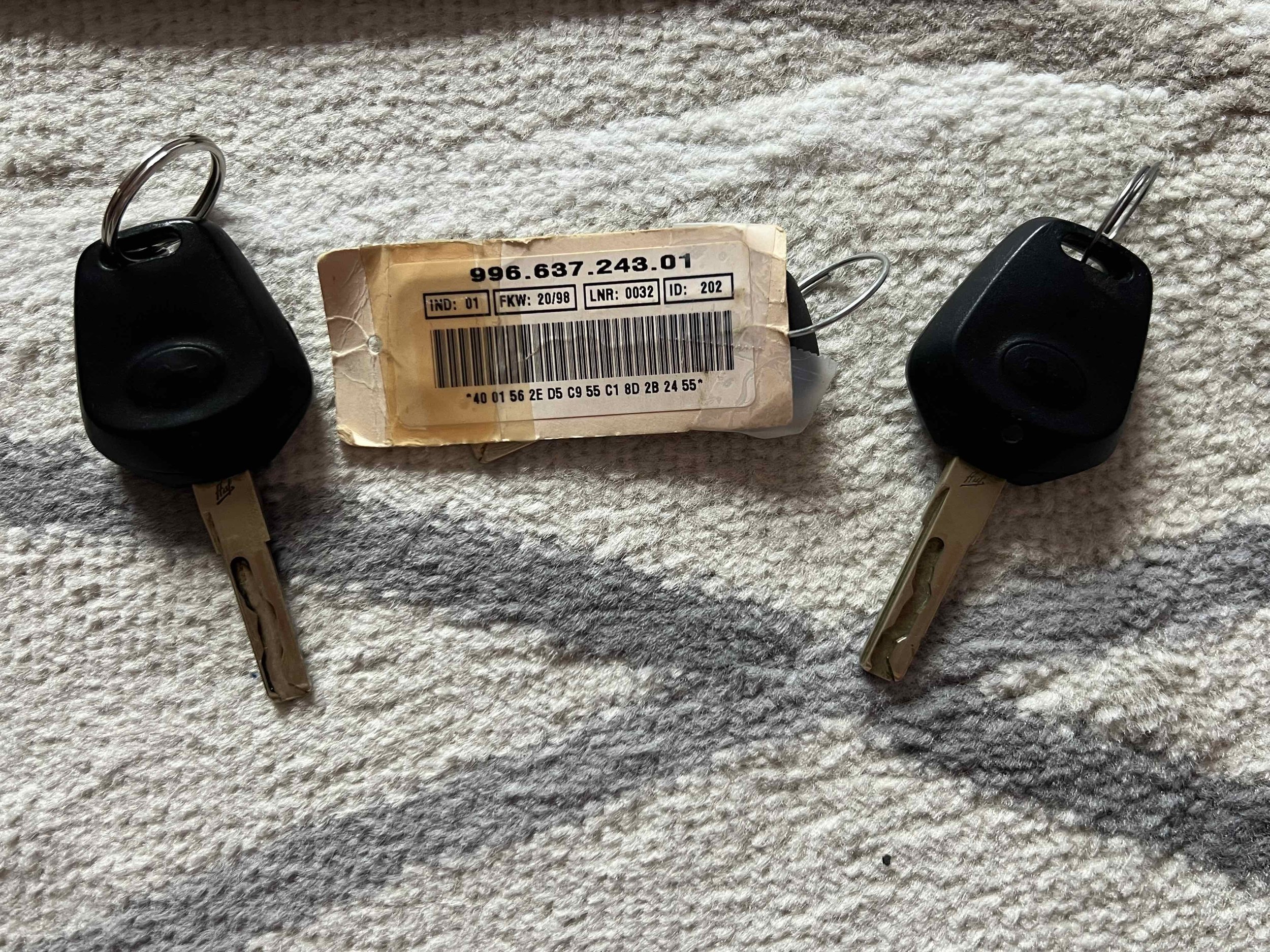 Two car key fobs with metal blades attached, lying on a textured fabric surface, with a worn, yellowed label between them.