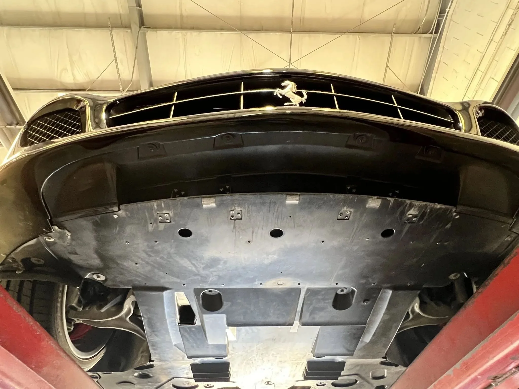 Underneath view of a Ferrari car with the logo visible on the front grill, showing the underside structure and suspension components.