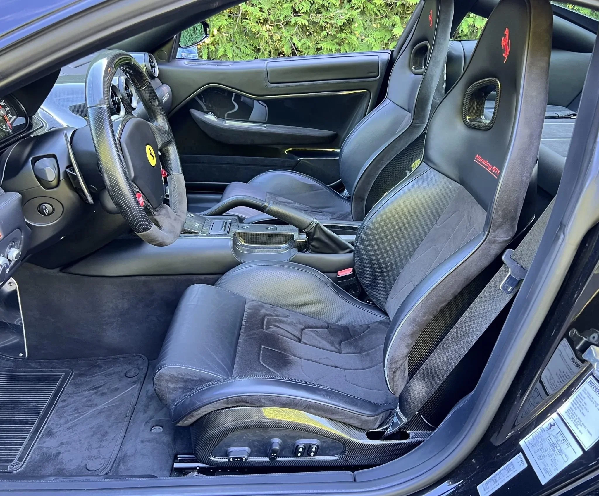Interior of a high-performance sports car with black seats, racing harnesses, and a carbon fiber steering wheel, reflecting a racing-oriented design.