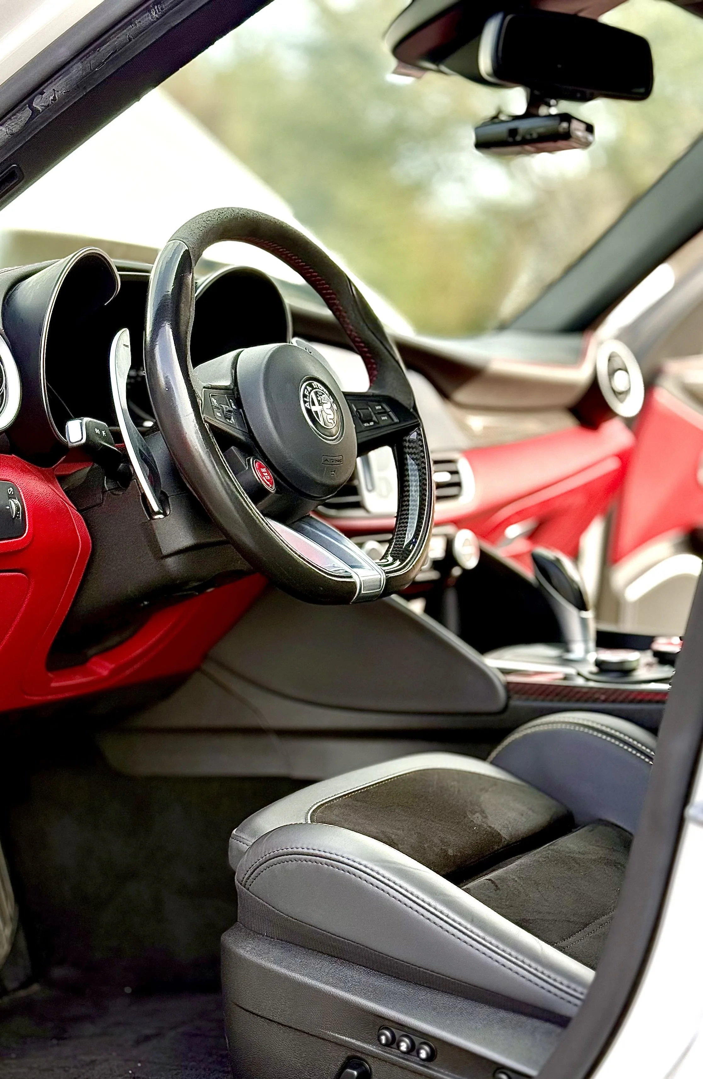 Interior of a luxury sports car with a black and red dashboard, steering wheel, gear shifter, and sports seat.