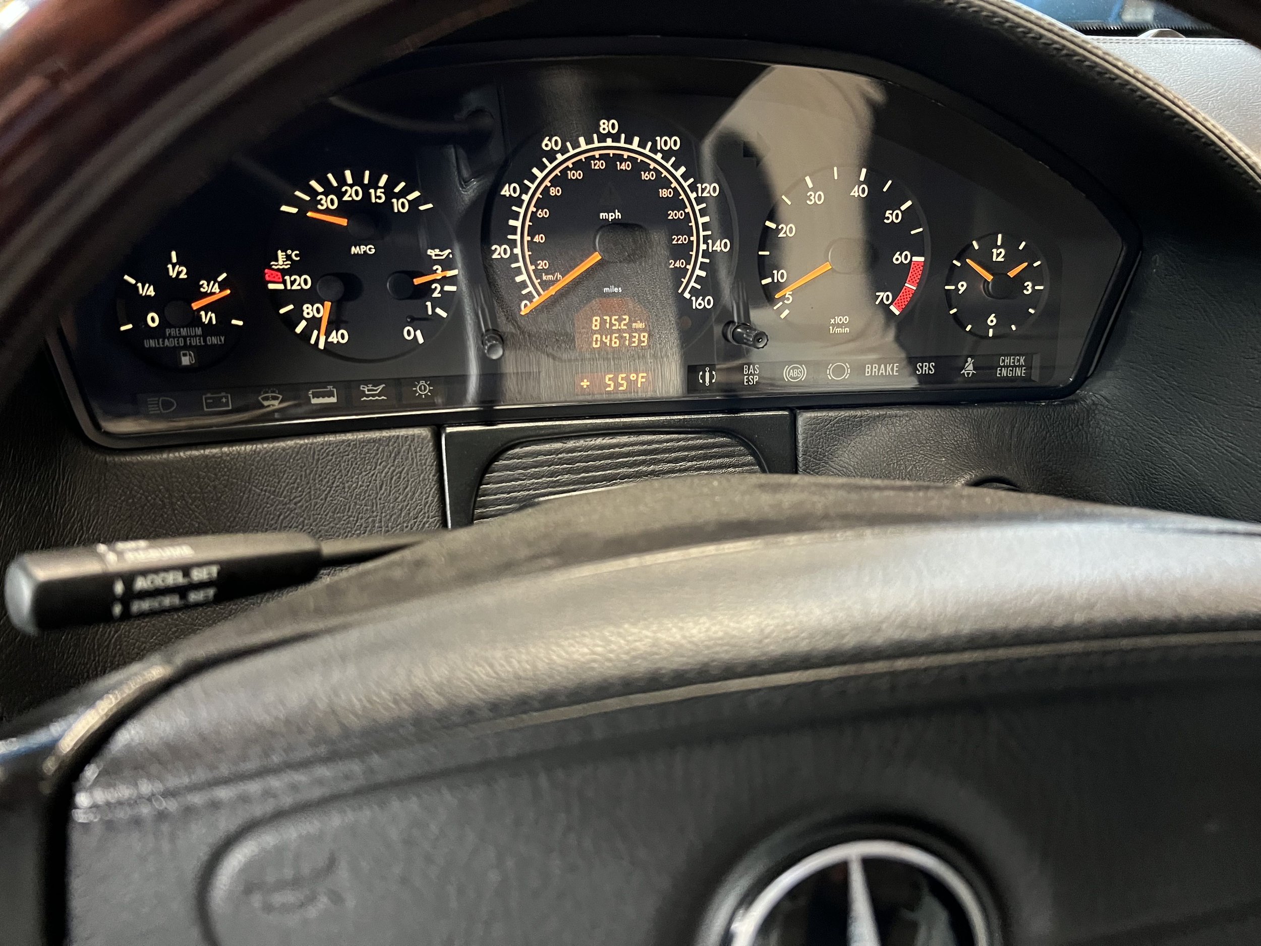 Car dashboard with speedometer, tachometer, fuel gauge, and various warning lights, visible through steering wheel.
