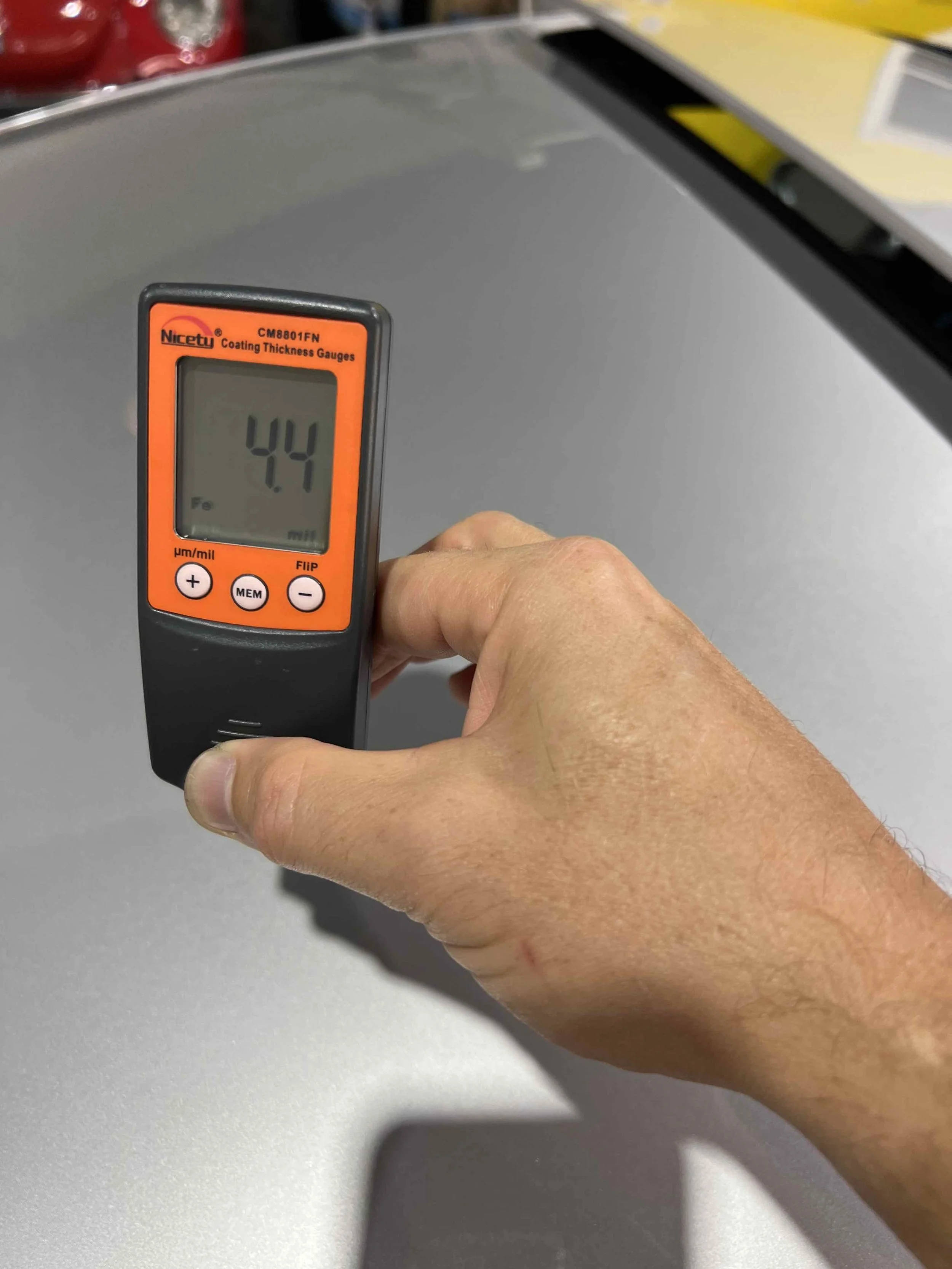 Hand holding a coating thickness gauge displaying a measurement of 4.4 micrometers.