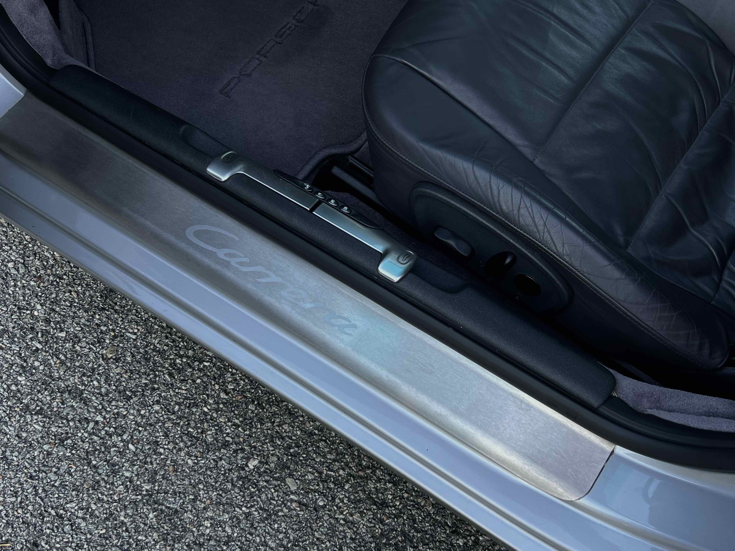 Close-up of the door sill and interior of a silver Porsche Carrera, featuring the Carrera branding on the door sill and a black leather seat.