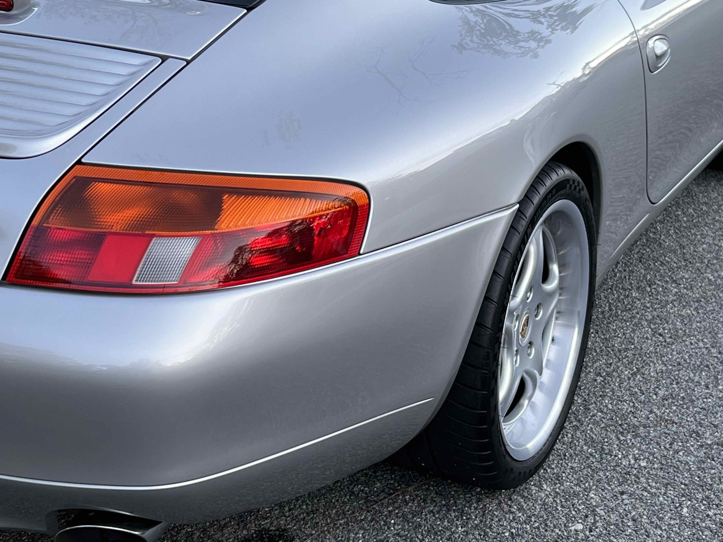 Close-up of the rear of a silver Porsche sports car, showing the tail light, rear wheel, and part of the body.