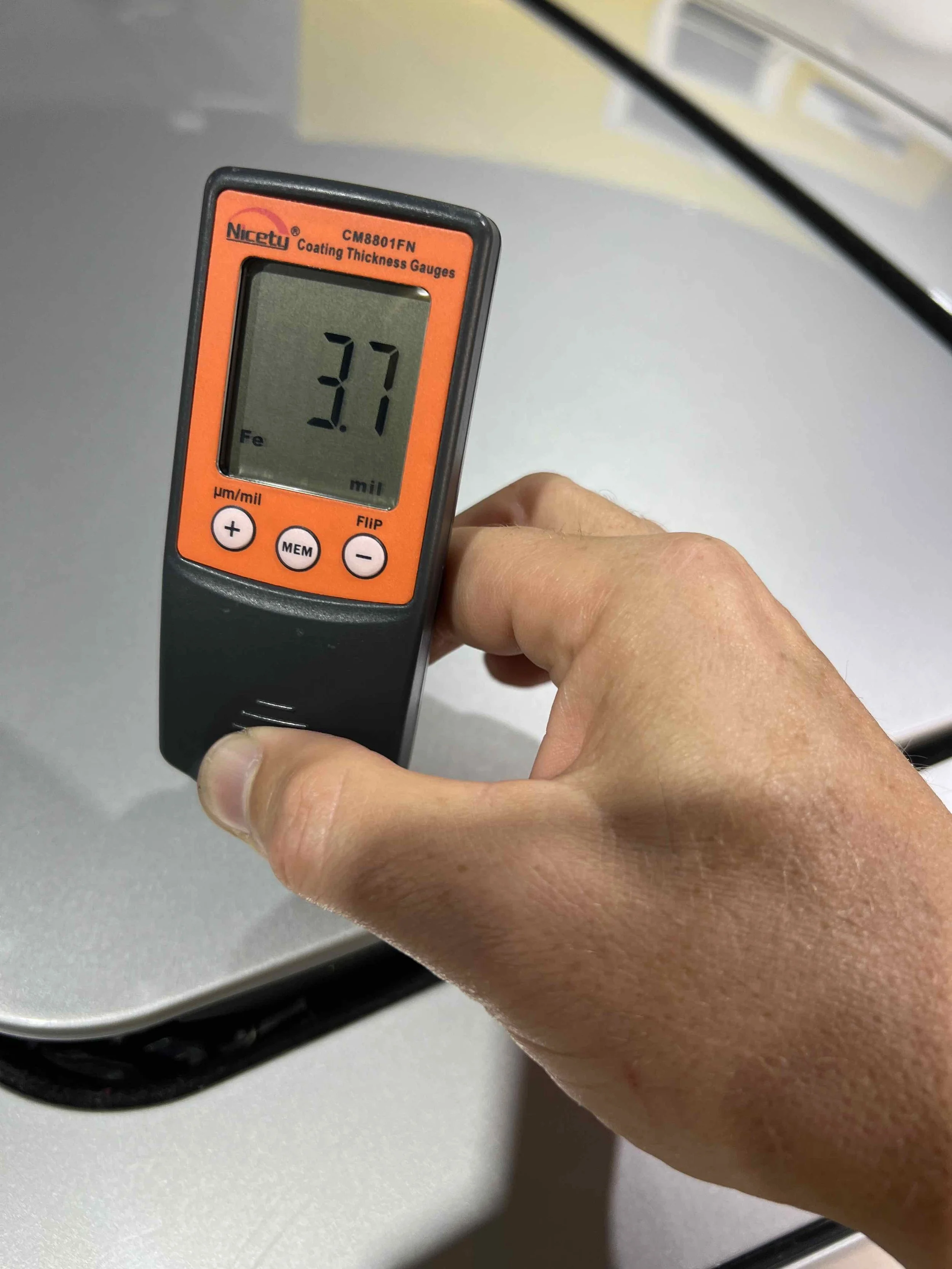 A hand holding a coating thickness gauge displaying a reading of 3.7 mils.