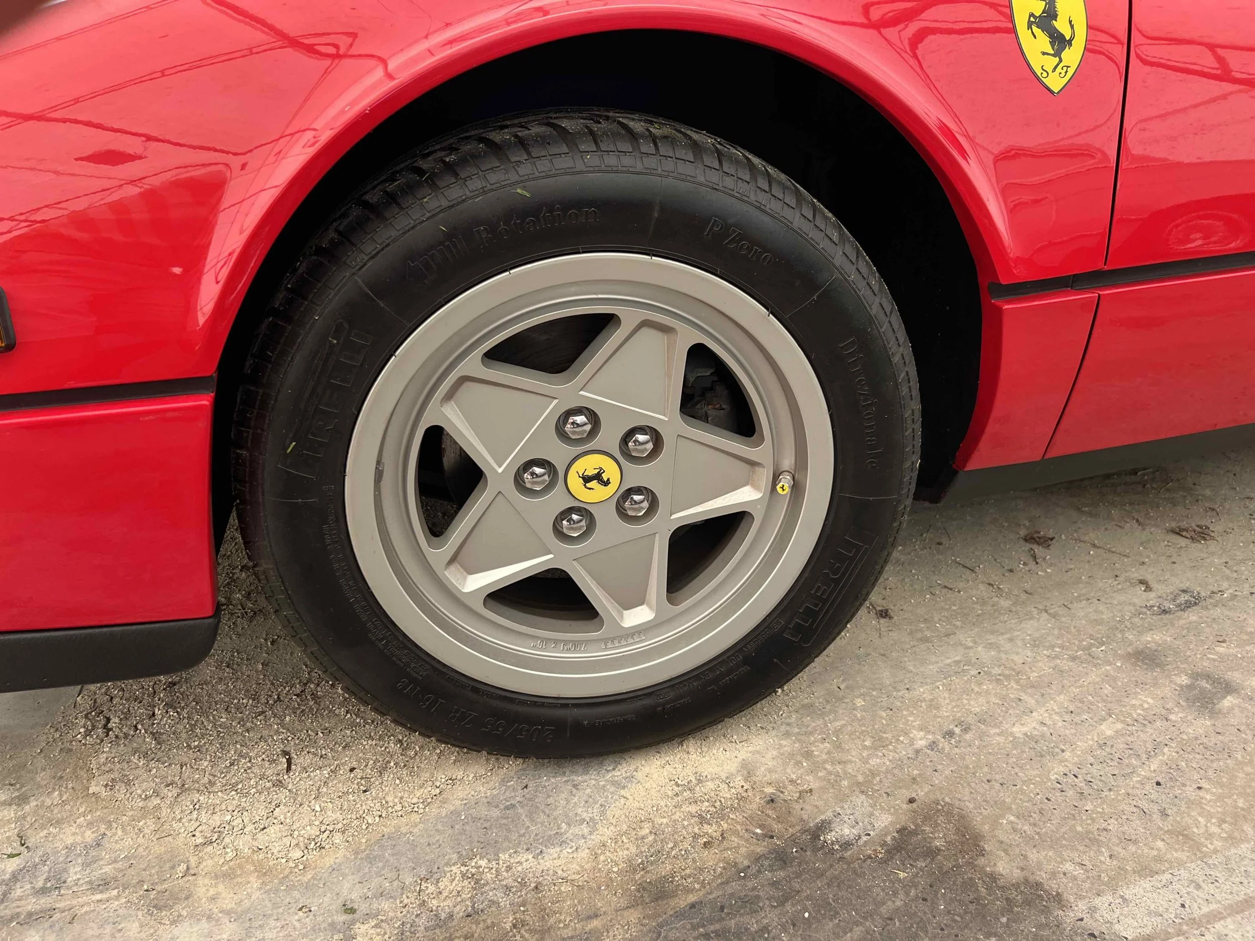 Close-up of a red Ferrari sports car wheel with a silver rim and yellow Ferrari logo center cap. The tire has markings including 'Pirelli' and 'Tauri'.