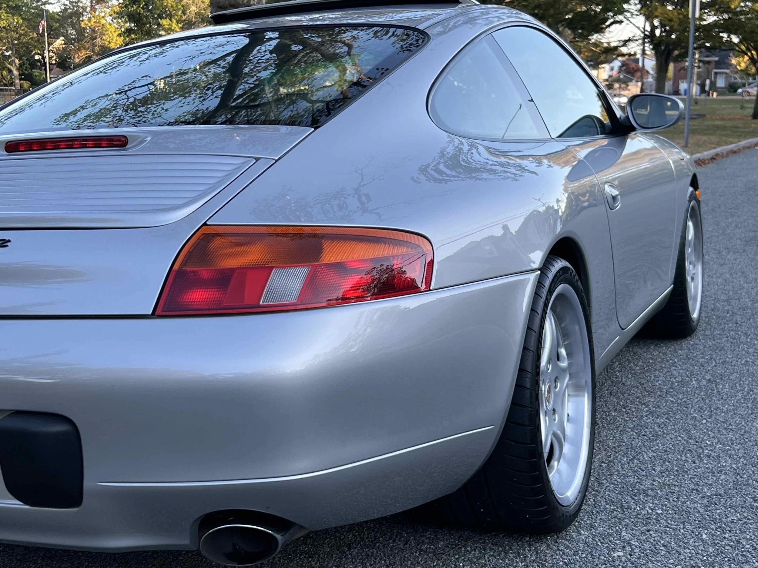 Silver sports car parked on a street with trees and houses in the background, showing the rear and side view.