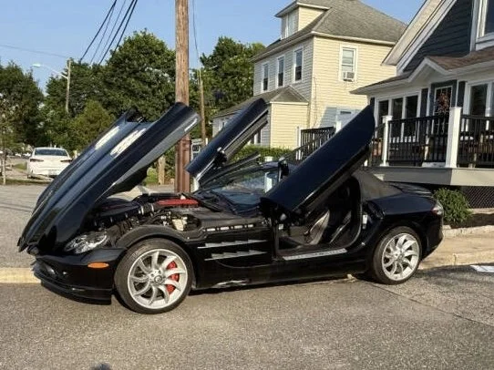 Black 2008 Mercedes Benz SLR McLaren Roadster with open doors against a building door 