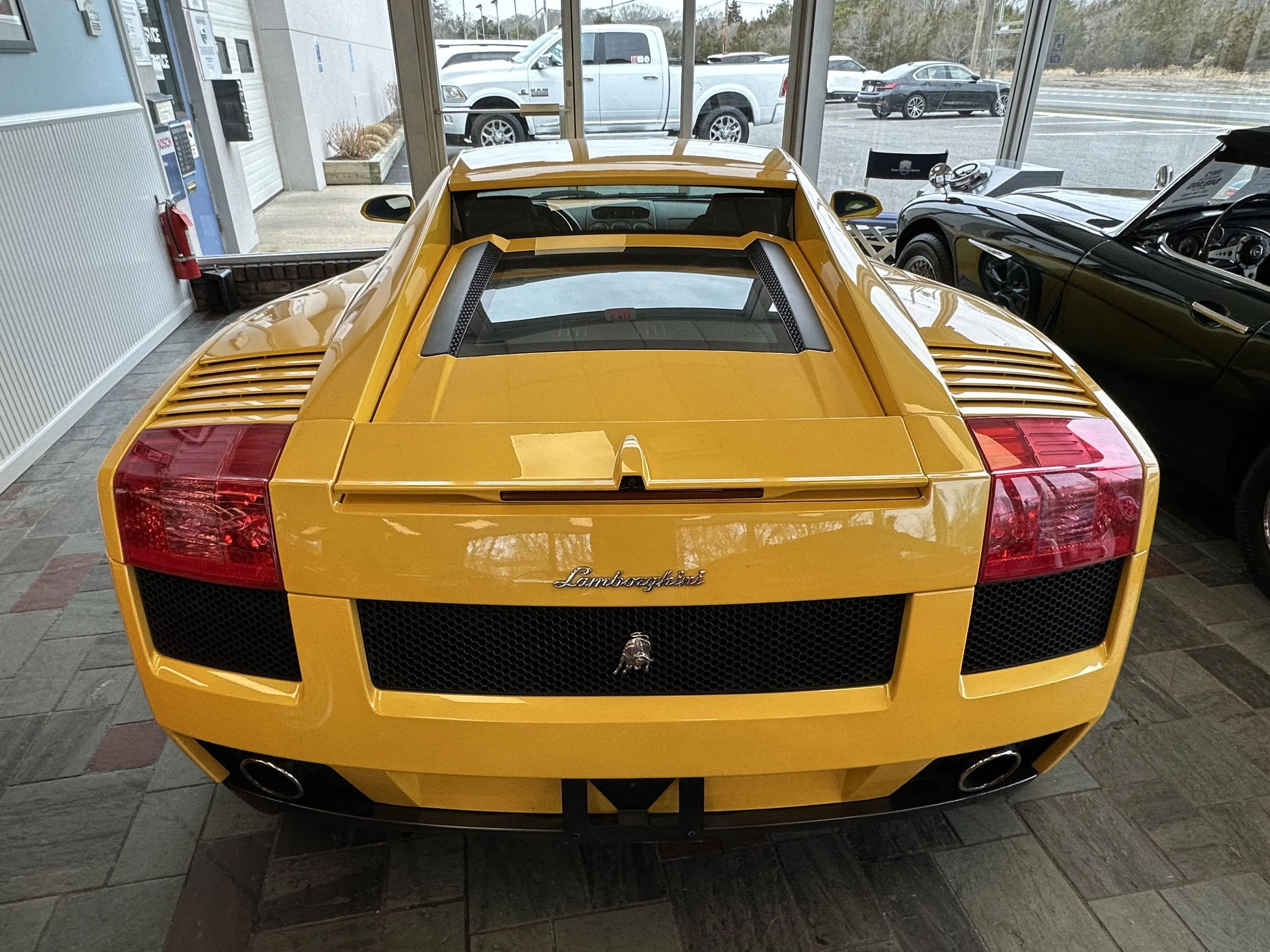 A yellow Lamborghini sports car inside a showroom, with large windows showing outside parking lot and other vehicles.