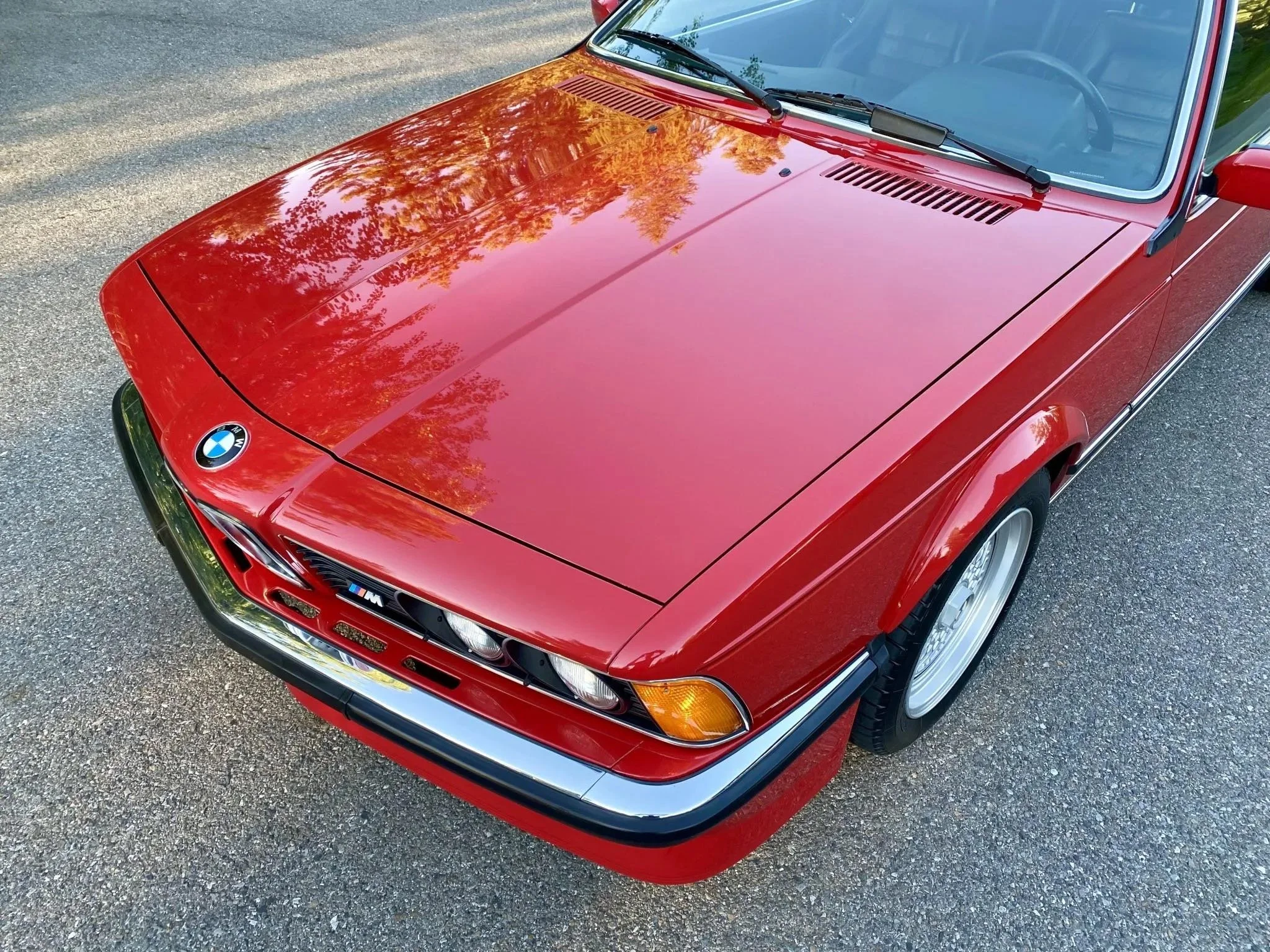 Red vintage BMW M car parked on asphalt, viewed from above, showing the front and part of the windshield.