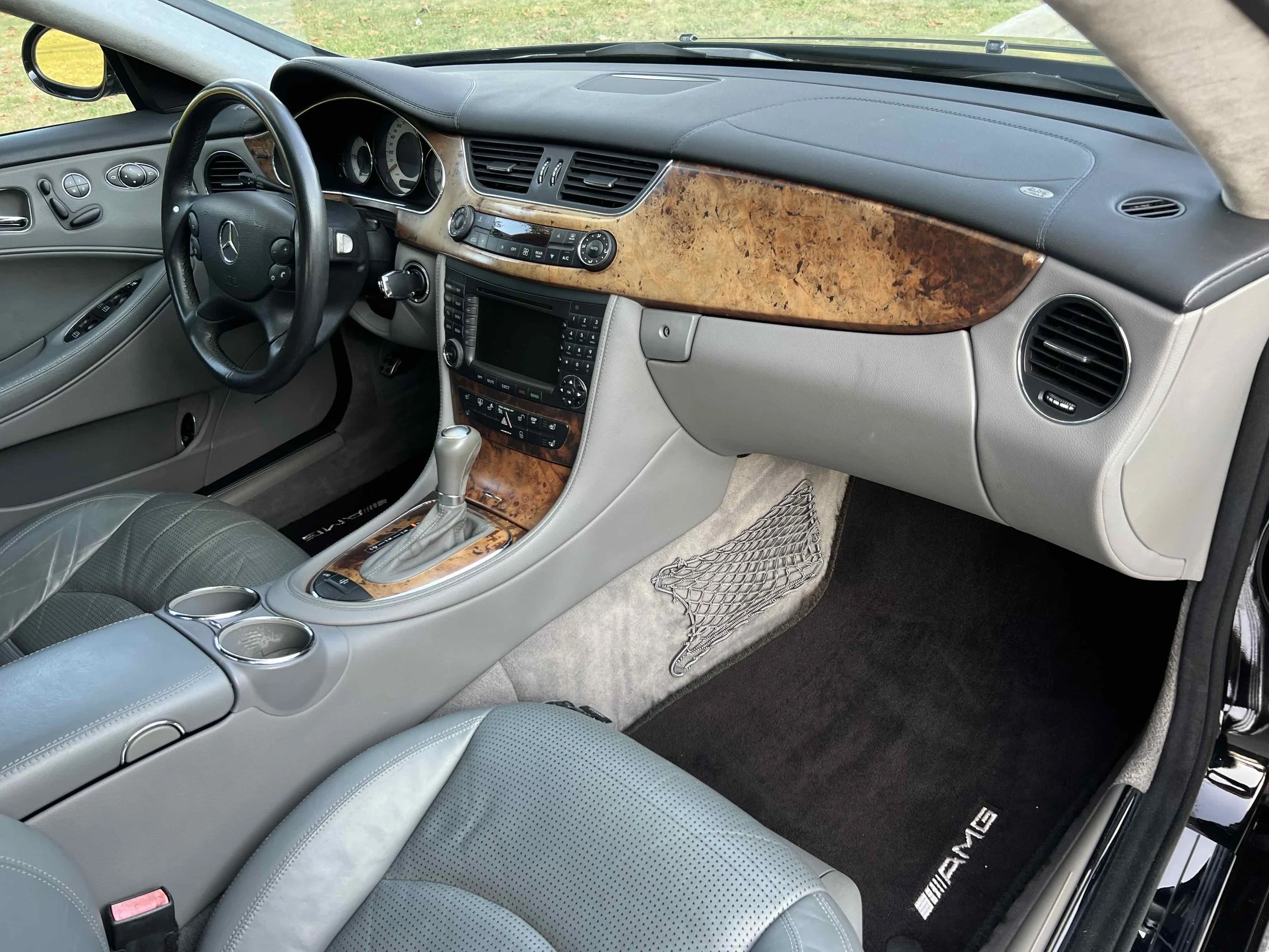 Interior of a luxury Mercedes-Benz vehicle with wood grain accents, leather seats, and an AMG branded floor mat.