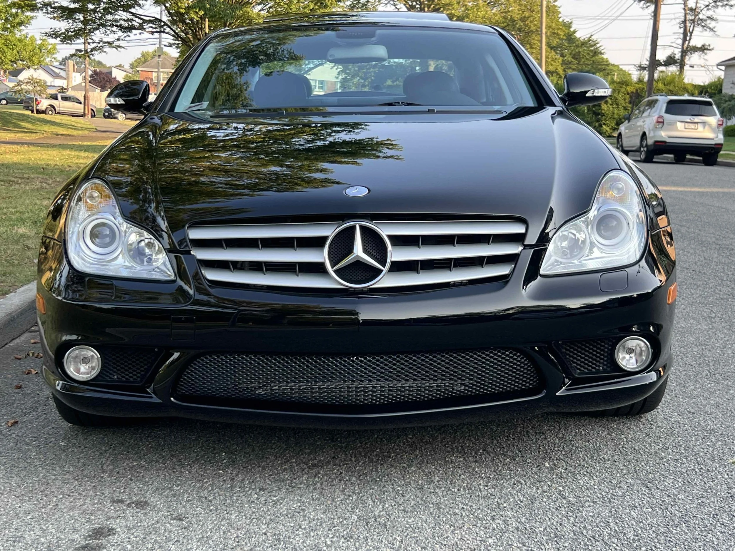 Black Mercedes-Benz car parked on the street with trees and other vehicles in the background