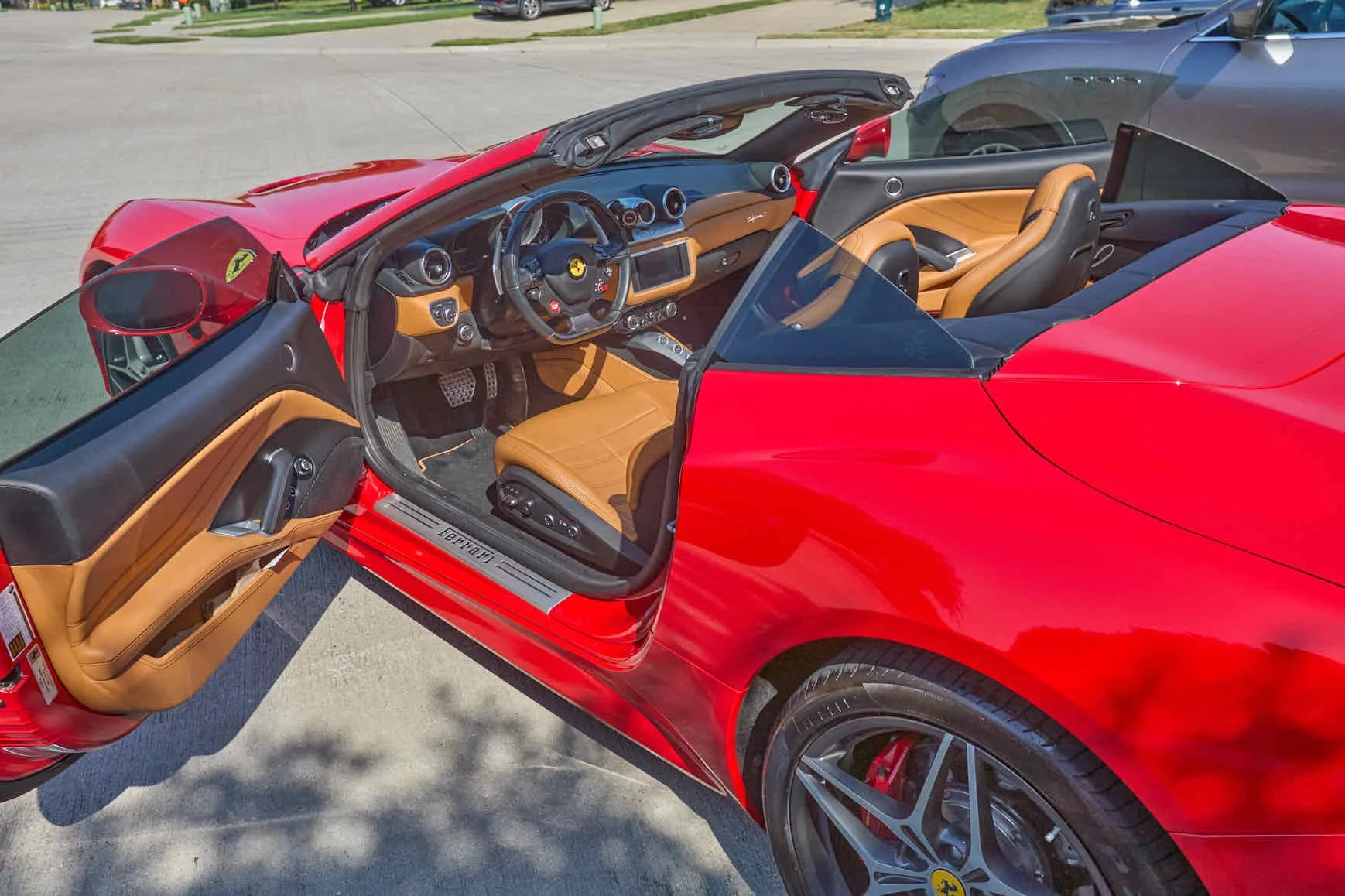 Red Ferrari convertible sports car with tan leather interior, parked with the driver's door open, showing the interior dashboard and seats.