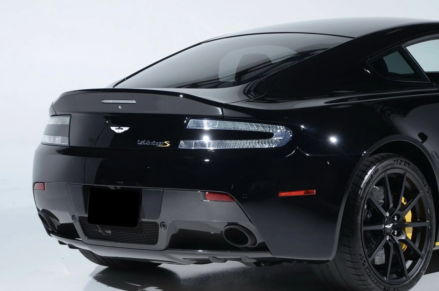 Rear view of a black Aston Martin V8 Vantage S sports car with carbon fiber accents and yellow brake calipers.