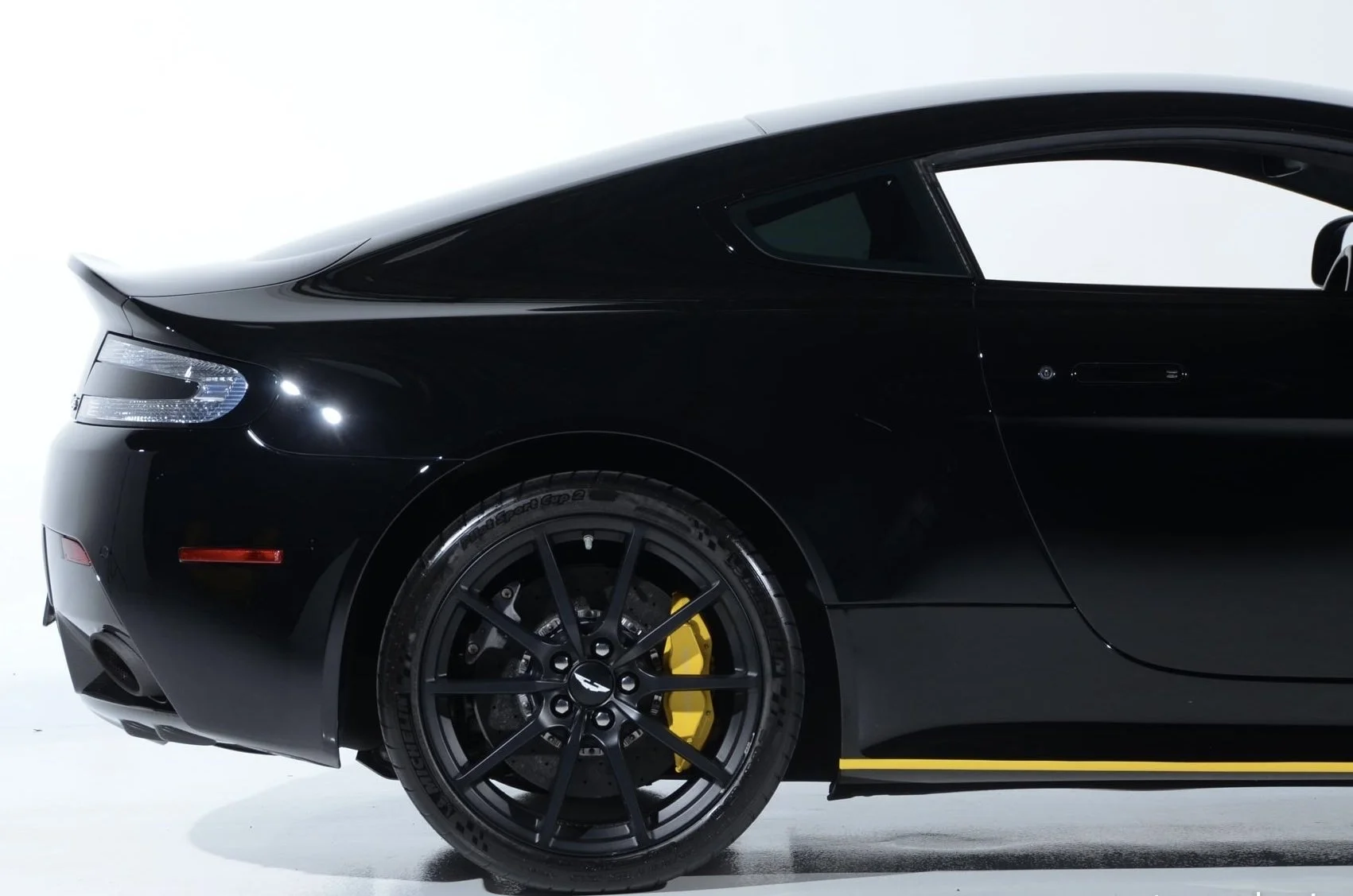 Close-up of the front side of a black sports car with sporty black wheels, yellow brake calipers, and sleek design.