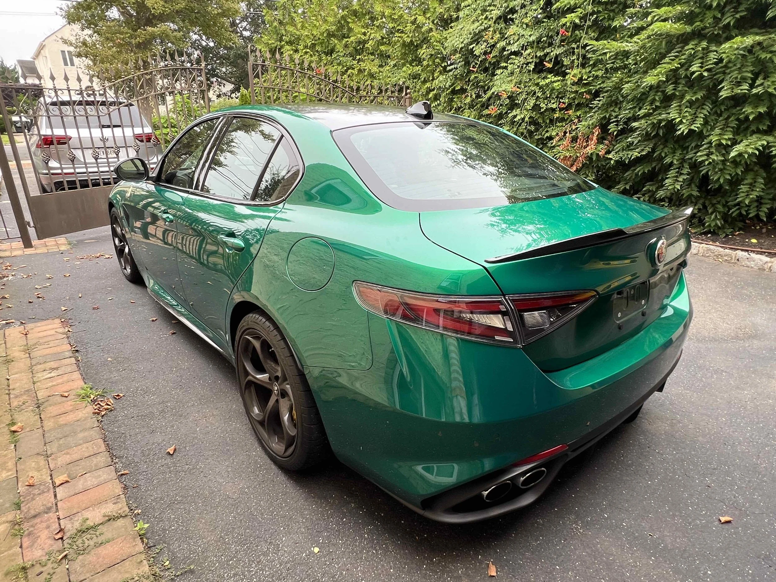 Green Alfa Romeo sedan parked in driveway near a gate and greenery.