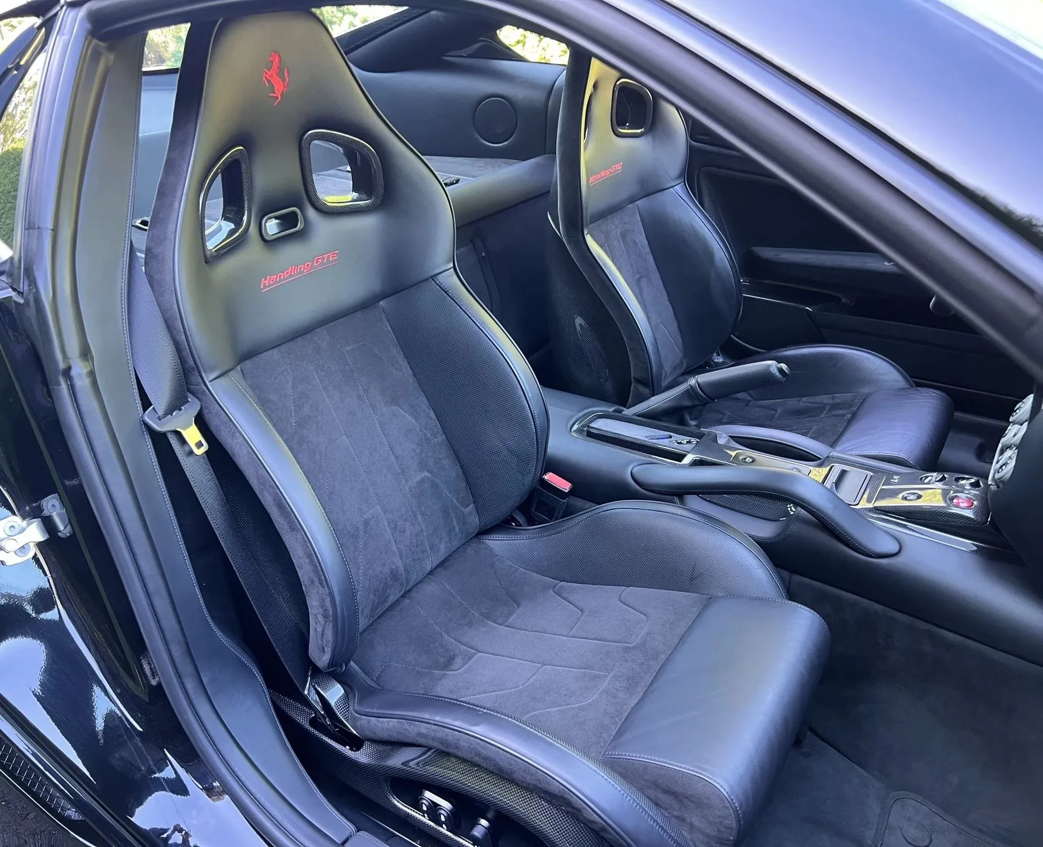 Interior of a sports car showing two racing bucket seats with 'Handling GTE' embroidered on the headrests, center console, shifter, and handbrake.