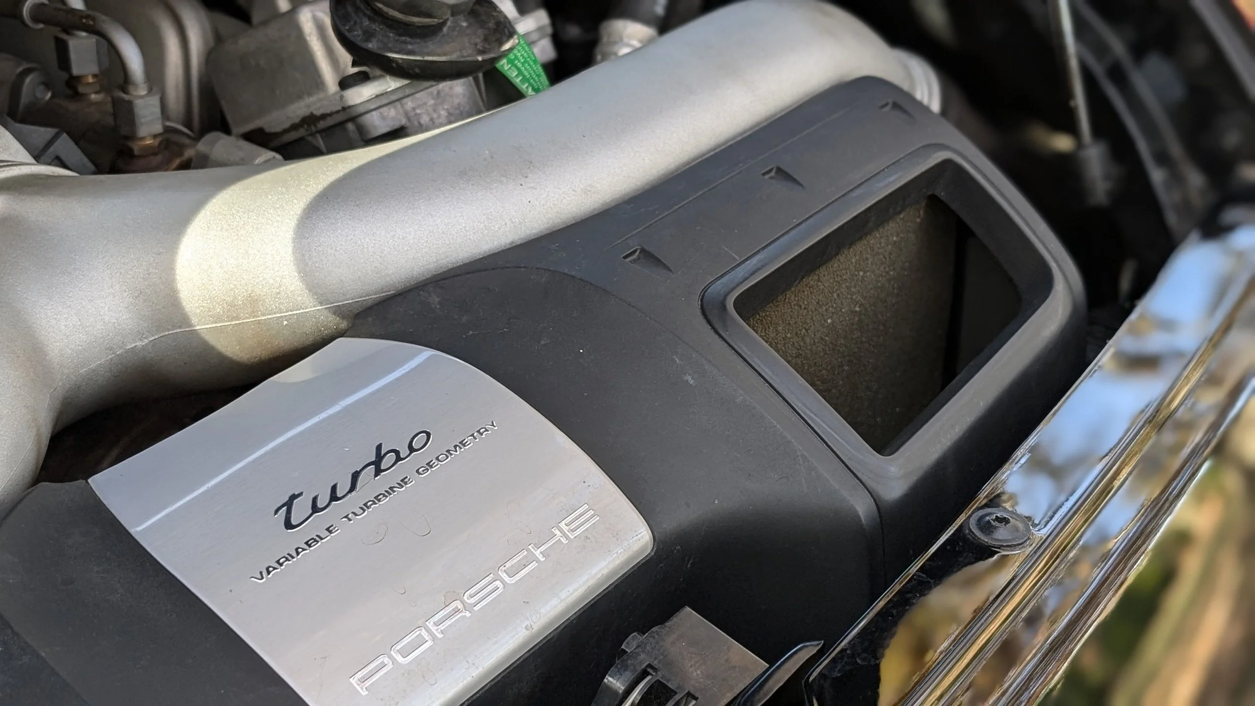 Close-up of a Porsche turbo engine with an aluminum cover labeled 'Turbo Variable Turbine Geometry' and the Porsche logo.