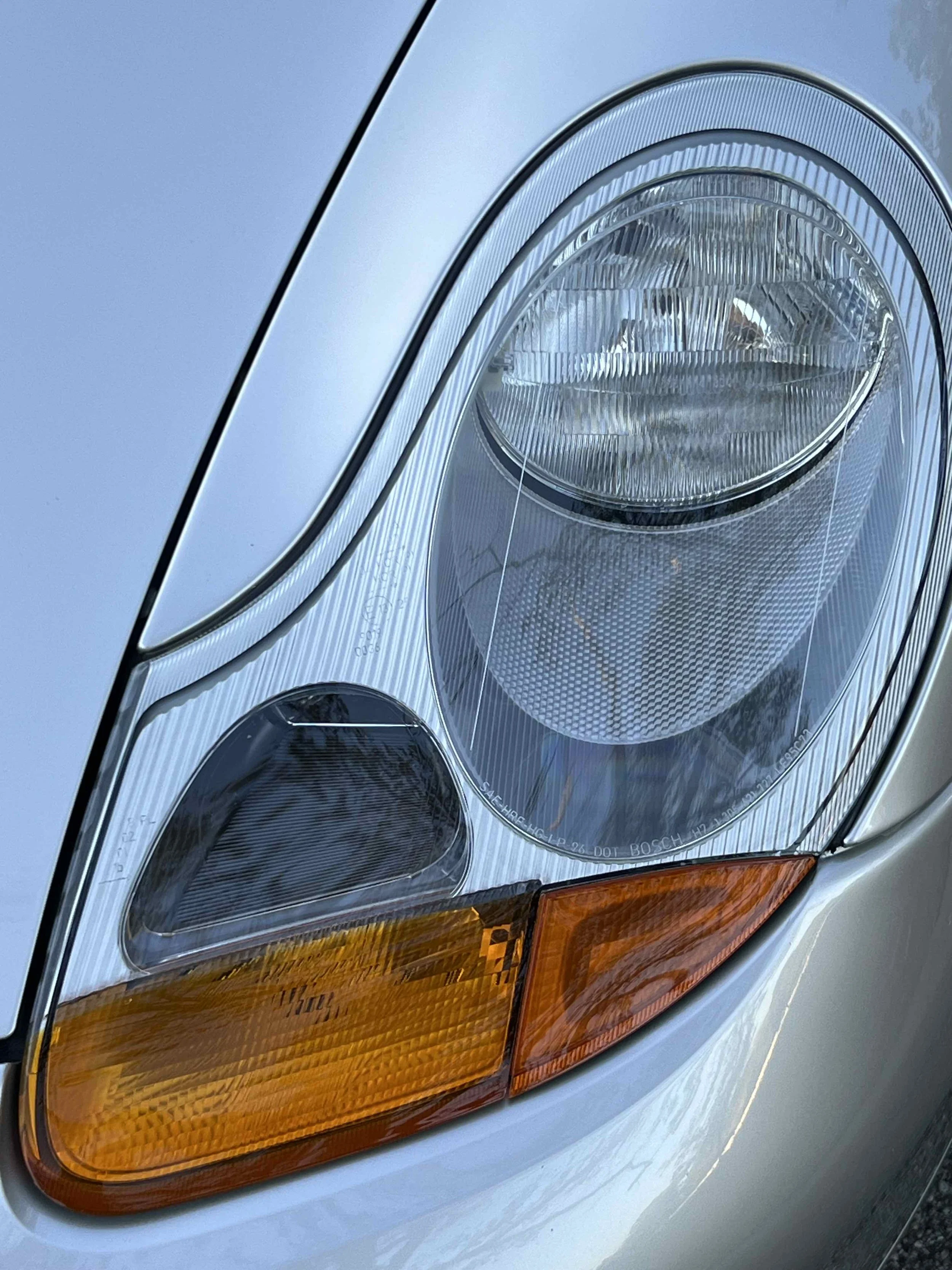 Close-up of a car's front headlight with orange turn signal, clear lens, and reflective surfaces.