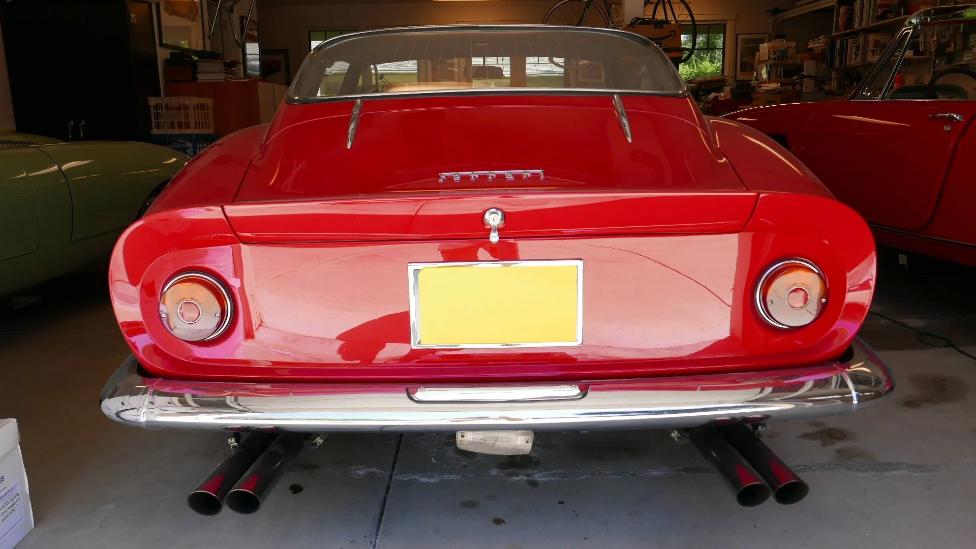Rear view of a classic red Ferrari car with dual exhaust pipes, round tail lights, in a garage.