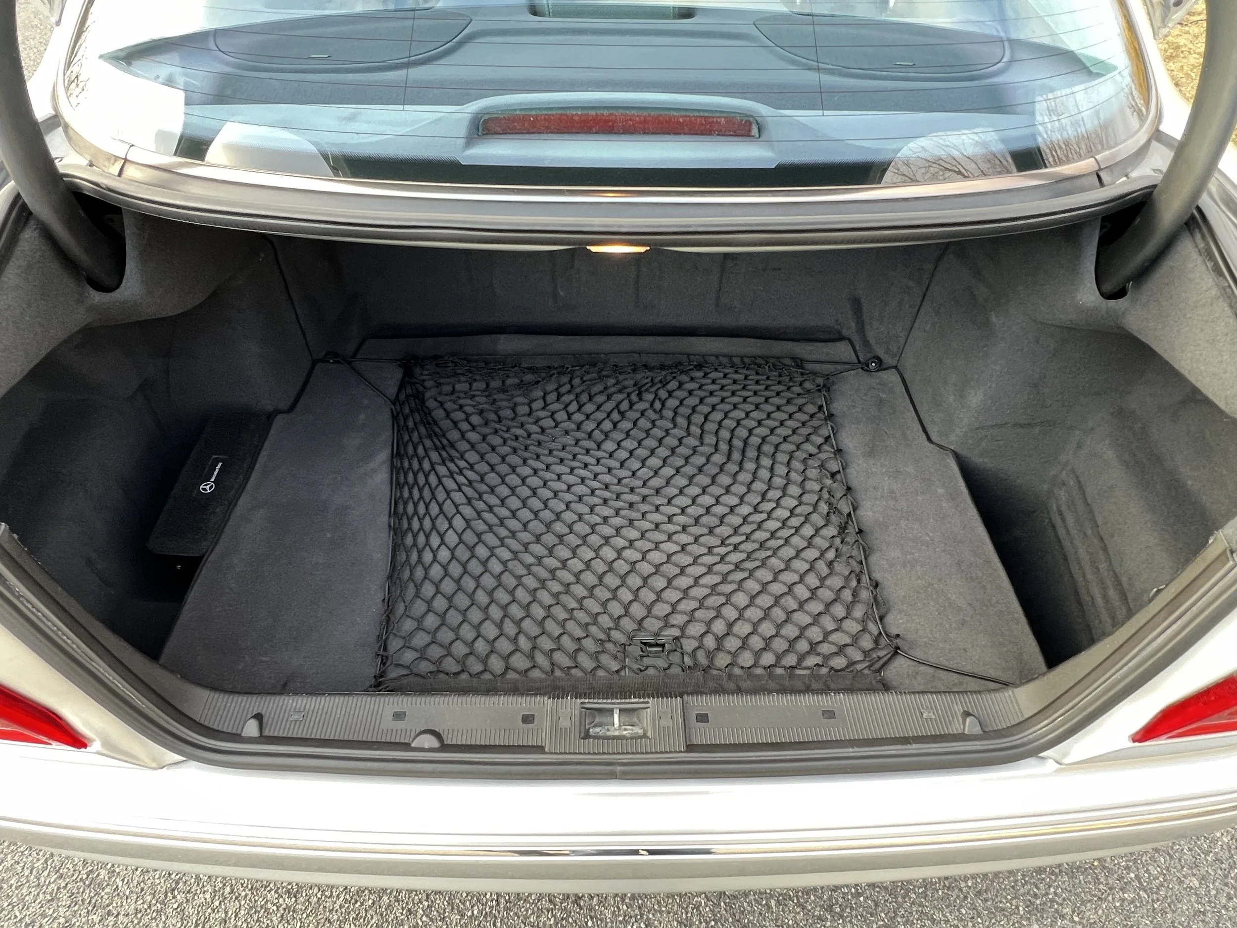The image shows the open trunk of a white car, revealing black interior with a netted storage area at the bottom.