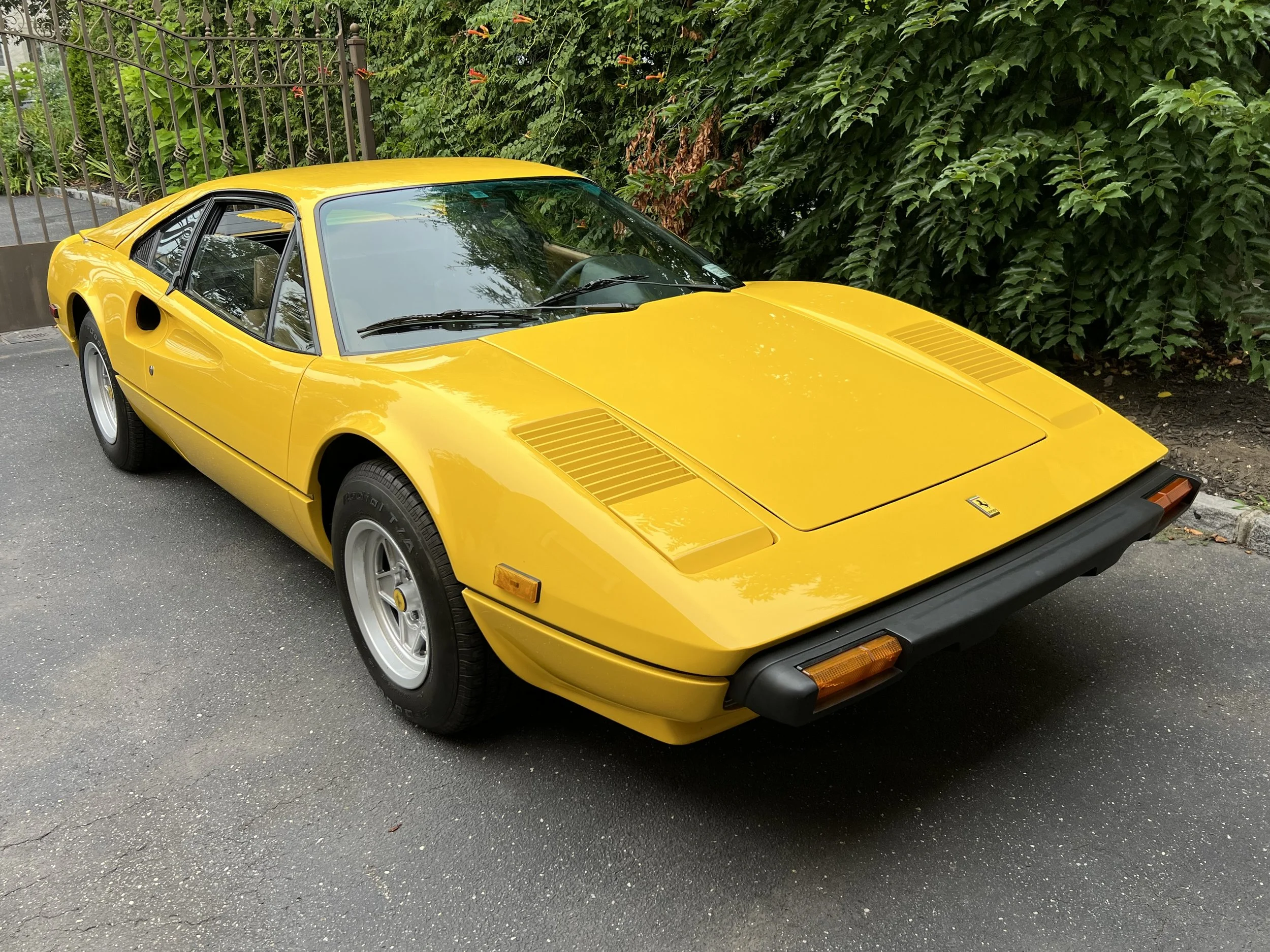 Yellow Ferrari 308 GTB on a driveway with trees in the background