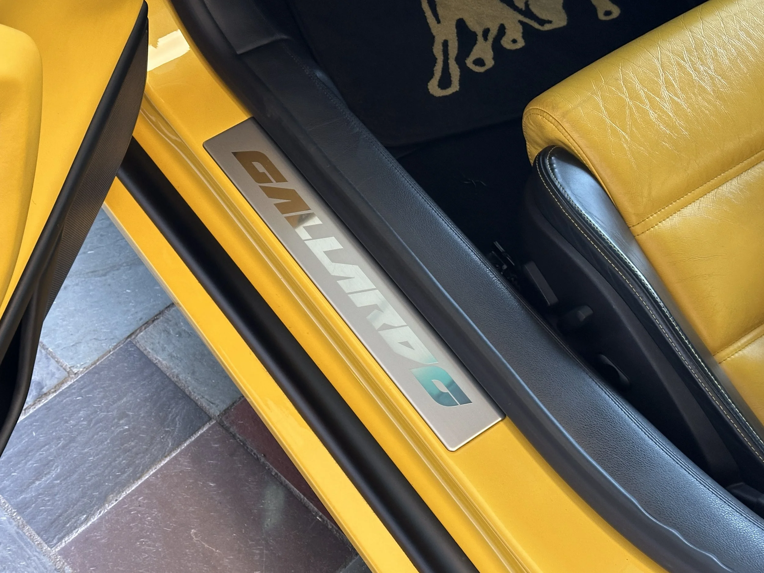 Close-up of a yellow Lamborghini with a silver Lamborghini logo on the door sill and a yellow leather car interior.