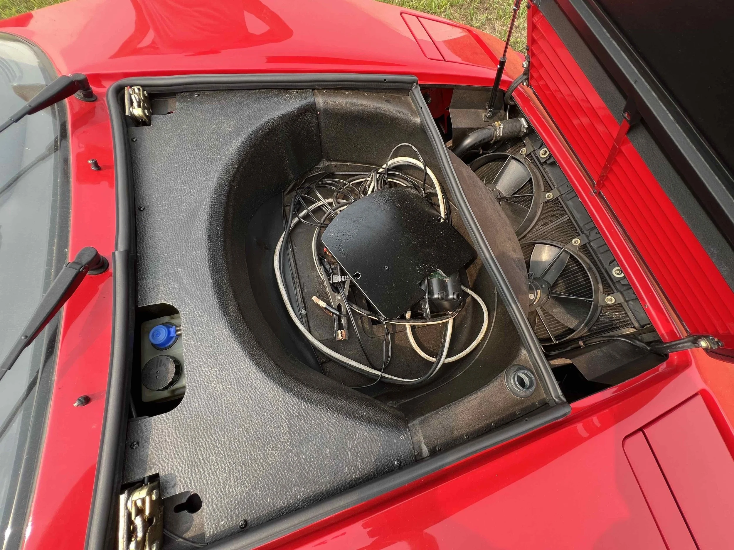 The engine compartment of a red sports car with two large fan radiators and a bundle of wires and electronic components.