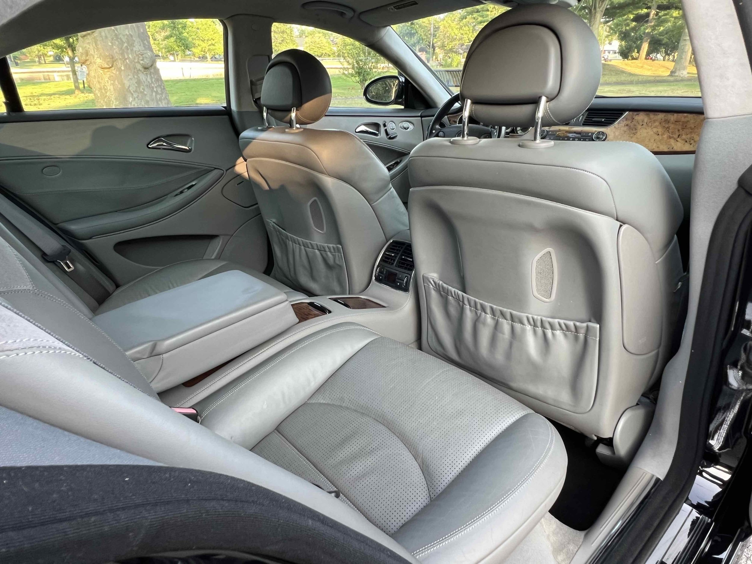 Interior of a luxury car showing leather seats, rear air vents, and a view of a park through the windows.
