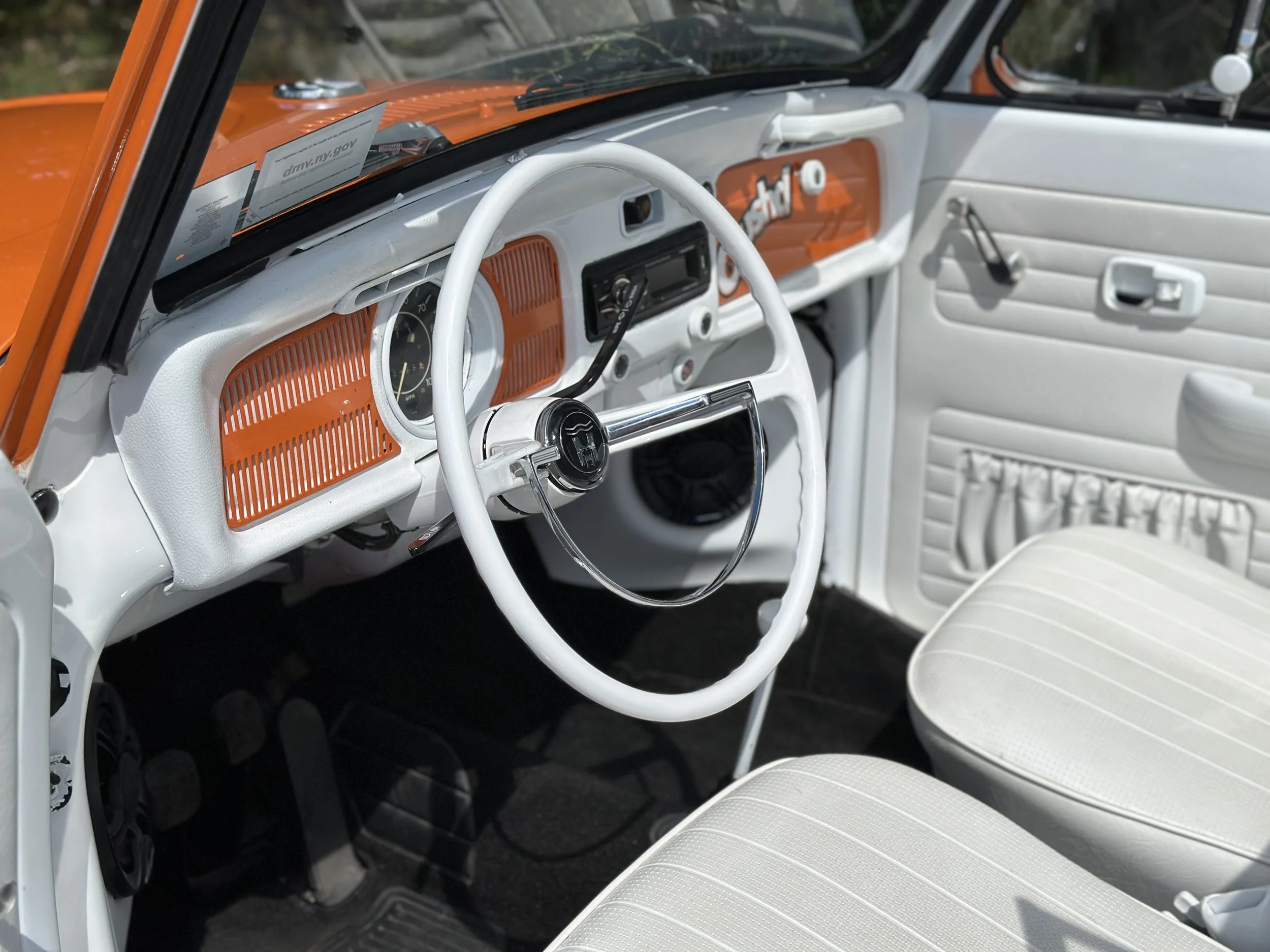 Interior of a vintage white and orange car, showing the steering wheel, dashboard, and passenger seat.