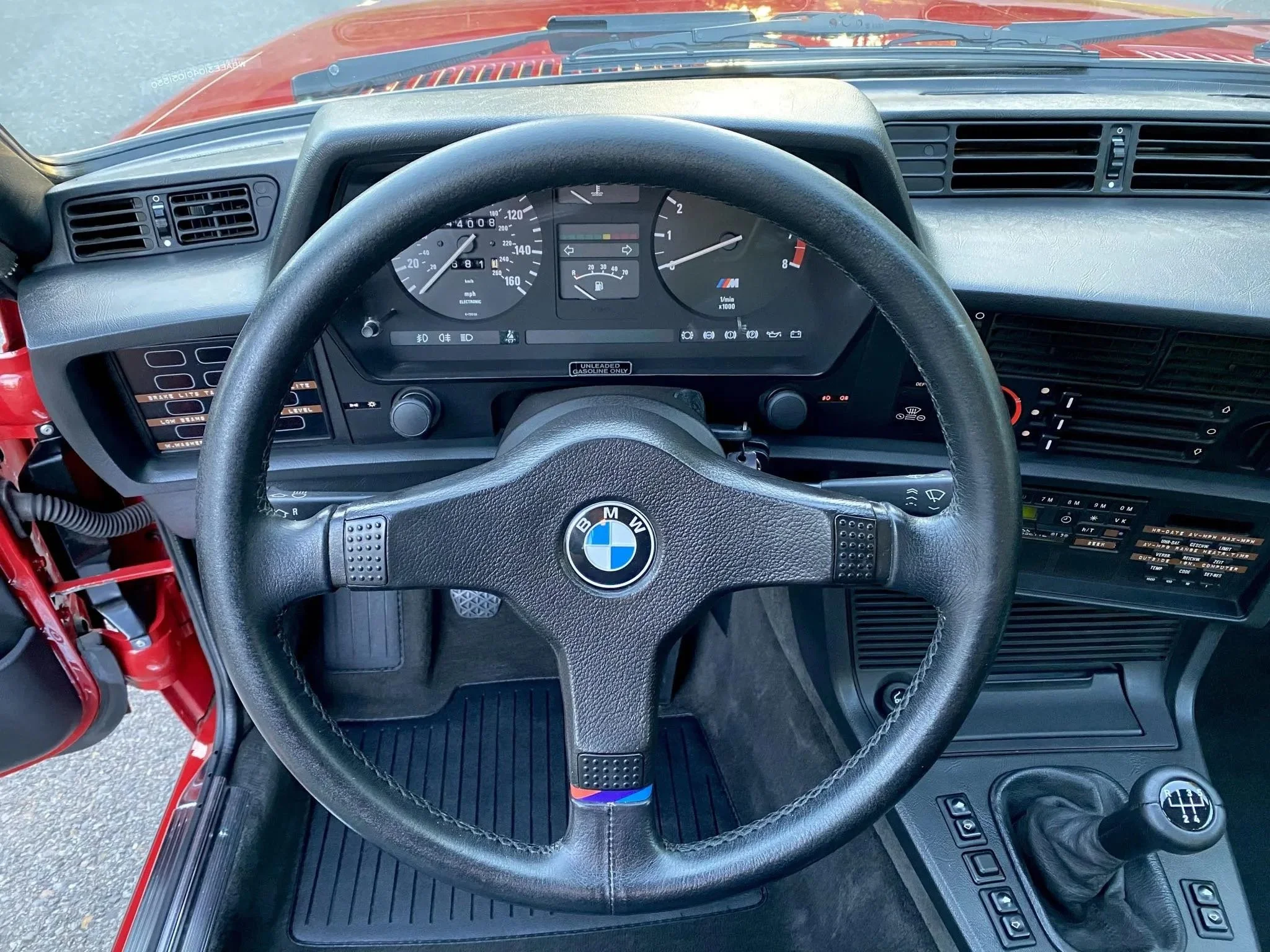 The interior of a vintage BMW car, showing the steering wheel with BMW logo, speedometer, tachometer, and various controls and dashboard features.