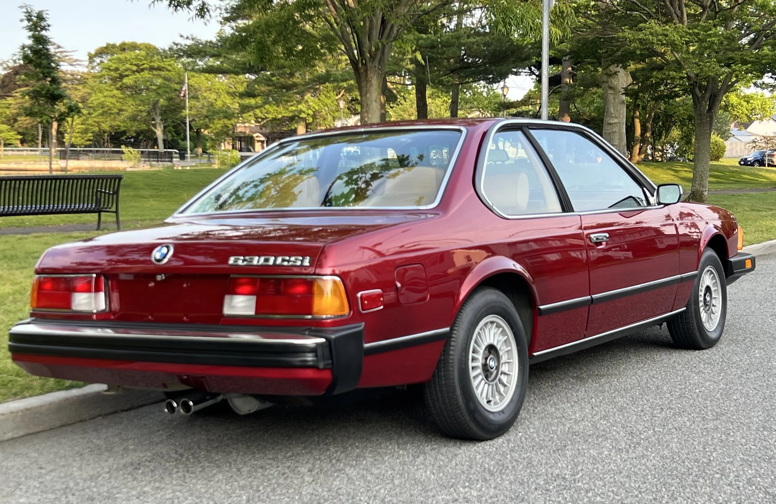 Ruby Red 1977 BMW 630 csi on display in park with trees and grass in background for sale at FlowHaus