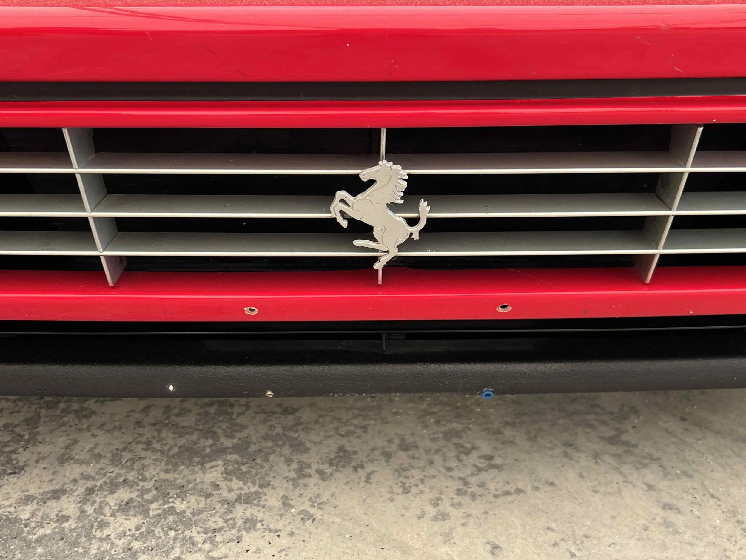 Close-up of a red Ferrari car front grille with the Ferrari prancing horse emblem in the center.