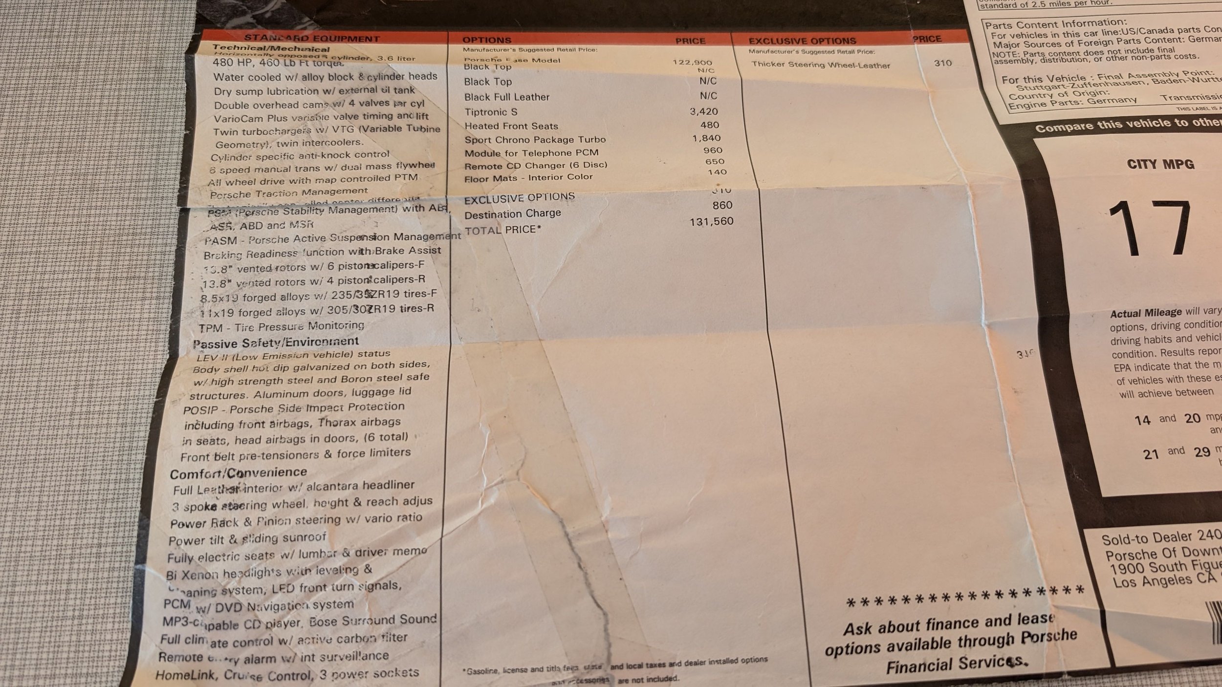 A close-up of a paper car information sheet with detailed specifications, options, prices, and safety features, partially folded and placed on a gray surface.